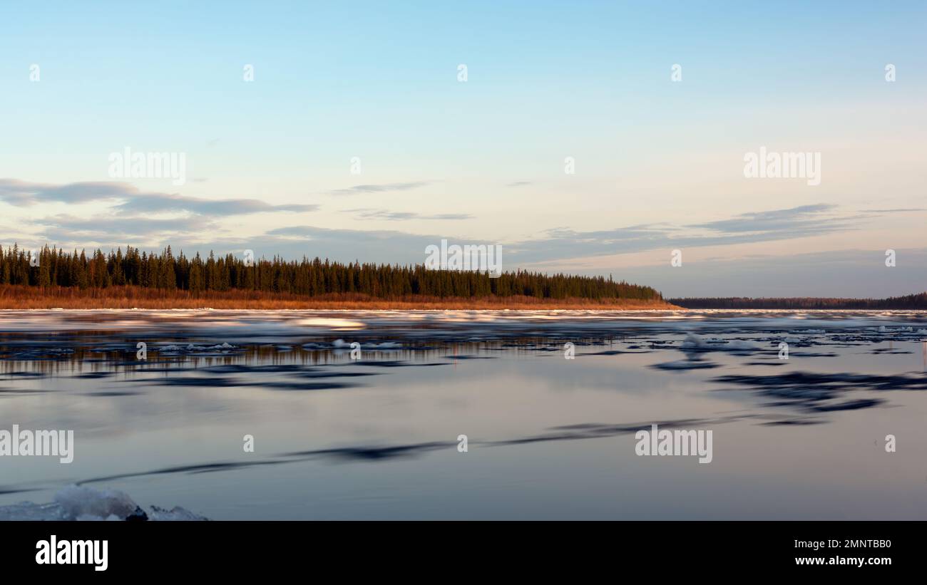 Die Bewegung des Wasserflusses mit Eis auf dem Eisfluß des Vilyui Flusses in Yakutia vor dem Hintergrund des Waldes am Abend. Langzeit Stockfoto