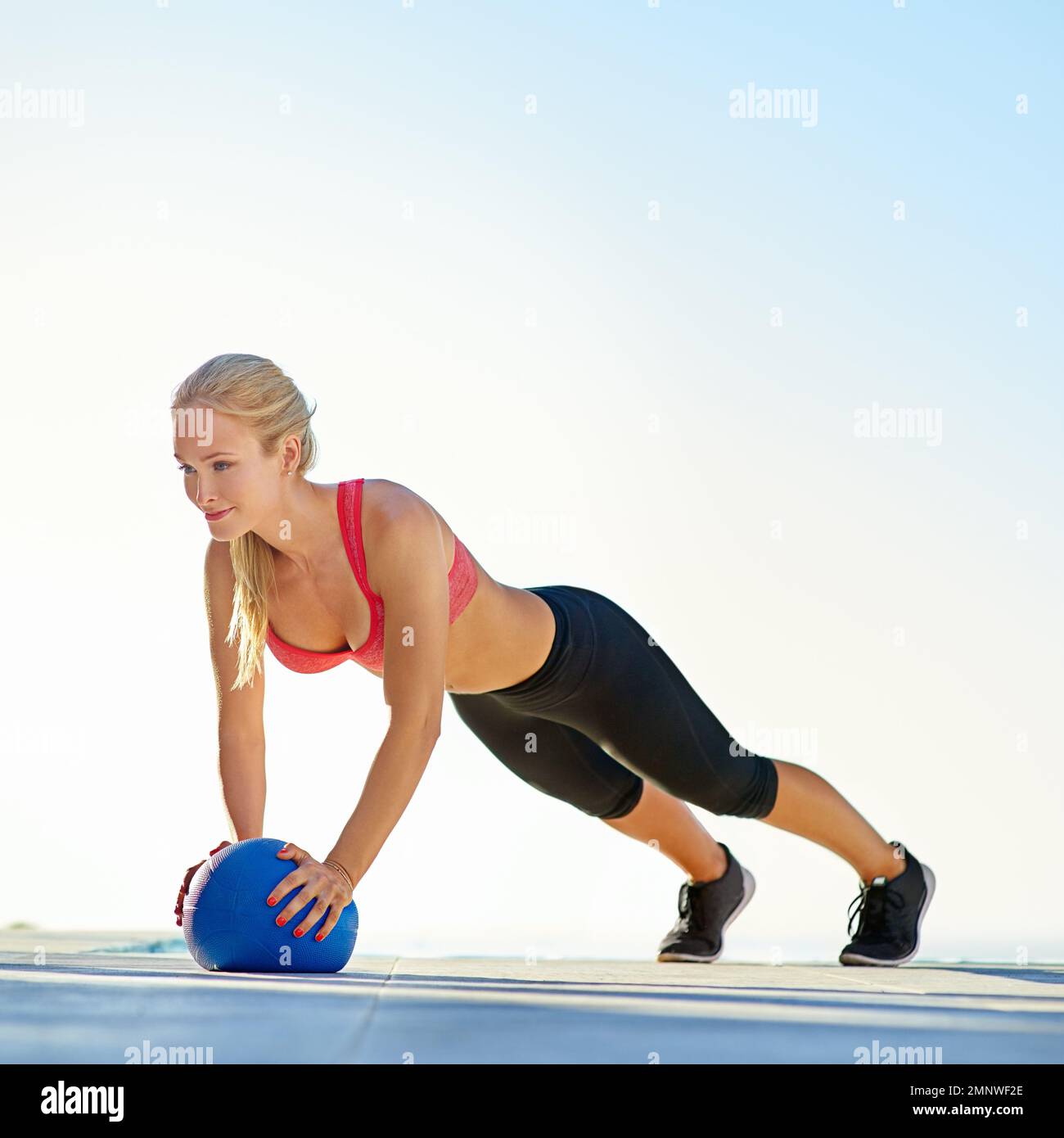 Auf Fitness fokussiert. Die volle Länge einer jungen Frau, die Liegestütze mit einem Medizinball macht. Stockfoto