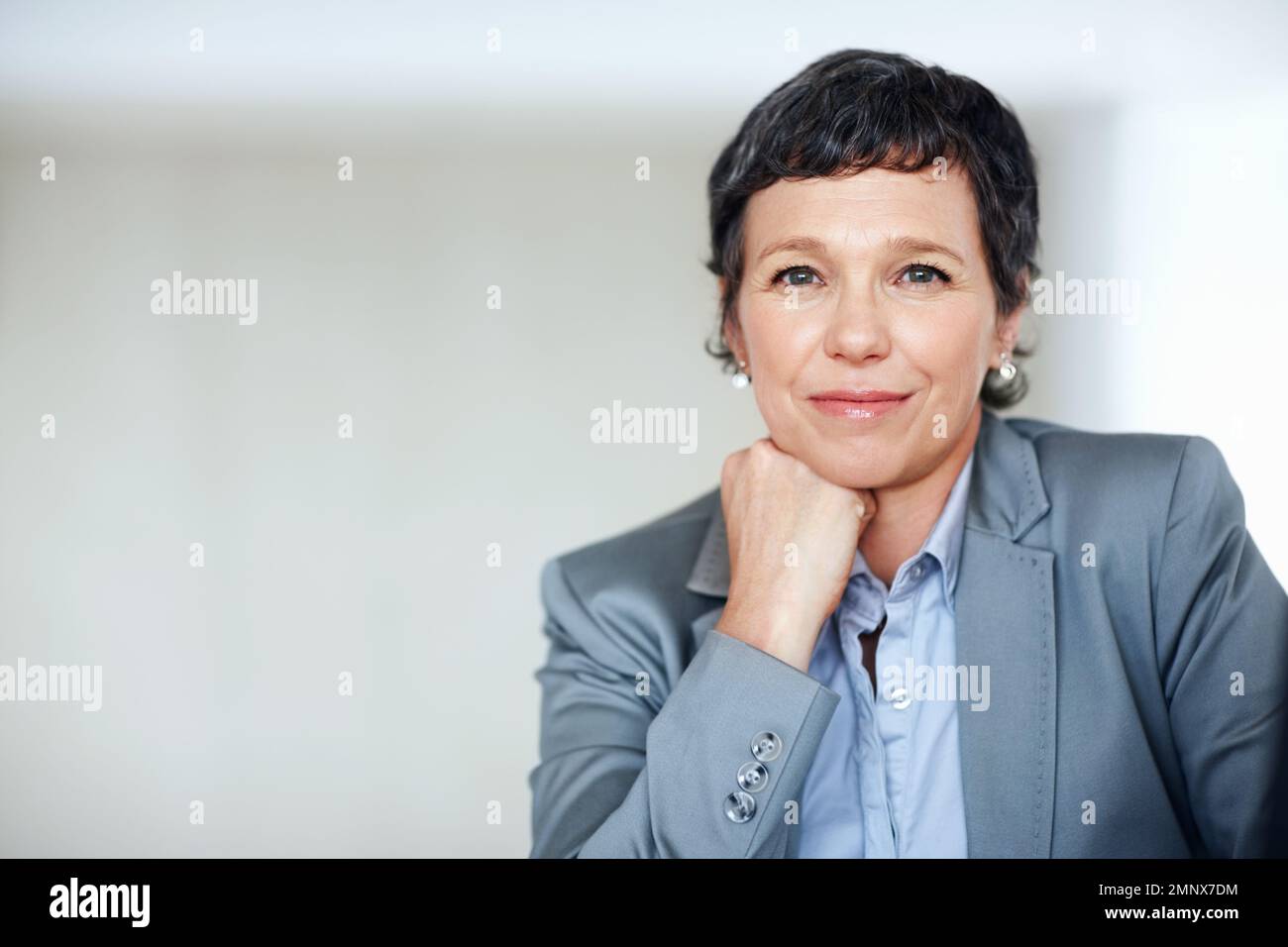 Raffinierte weibliche Führungskraft im Büro. Porträt einer anspruchsvollen, reifen Geschäftsfrau, die am Schreibtisch lächelt. Stockfoto
