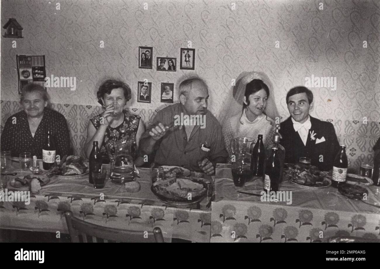 Vintage-Moment / Vintage-lustiger Moment / Vintage-Foto / Power of the Moment / magische Momente / Vintage-Essen / Essen / hausgemachte Vintage-Hochzeit aus den 1940er oder 1950er Jahren. Die Familienmitglieder sitzen hinter dem Tisch, der voll ist mit Essen, gegrilltem Hühnchen, Bier, Wein, leeren und vollen Gläsern und Flaschen, vollen Aschenbechern. Ein sehr glücklicher Moment. Schön? Braut glücklich? Ehemann? :D Stockfoto