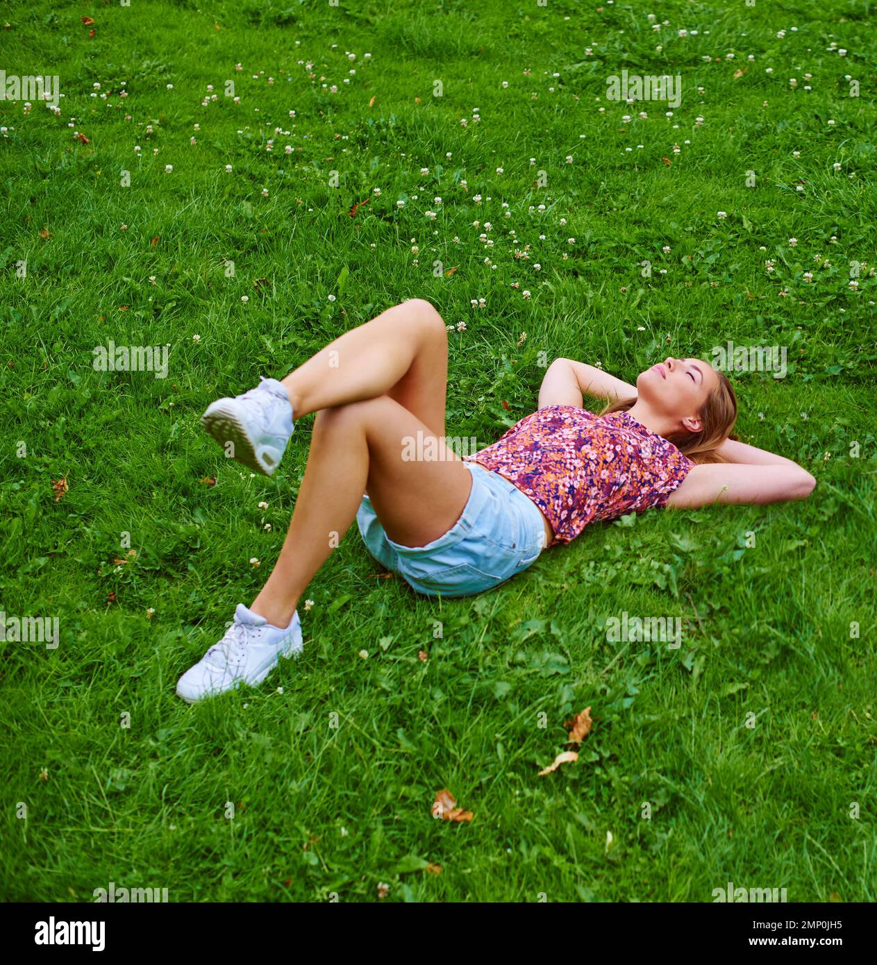 Sie genießt jeden Moment ihres Lebens. Eine junge Frau, die sich auf dem Gras in einem Park entspannt. Stockfoto