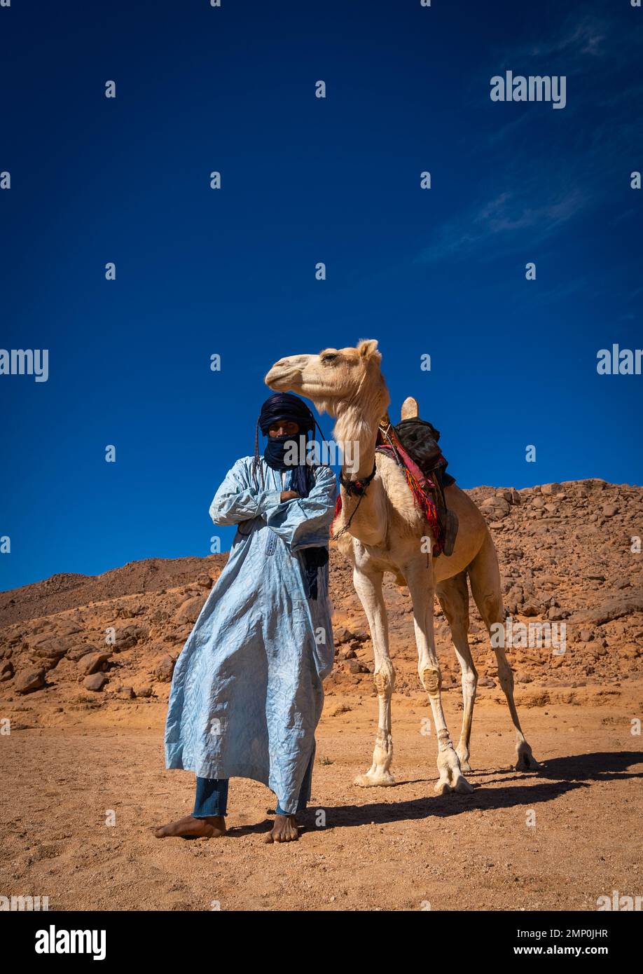 Tuareg-Mann steht vor seinem Kamel in der Wüste, Nordafrika, Tamanrasset, Algerien Stockfoto