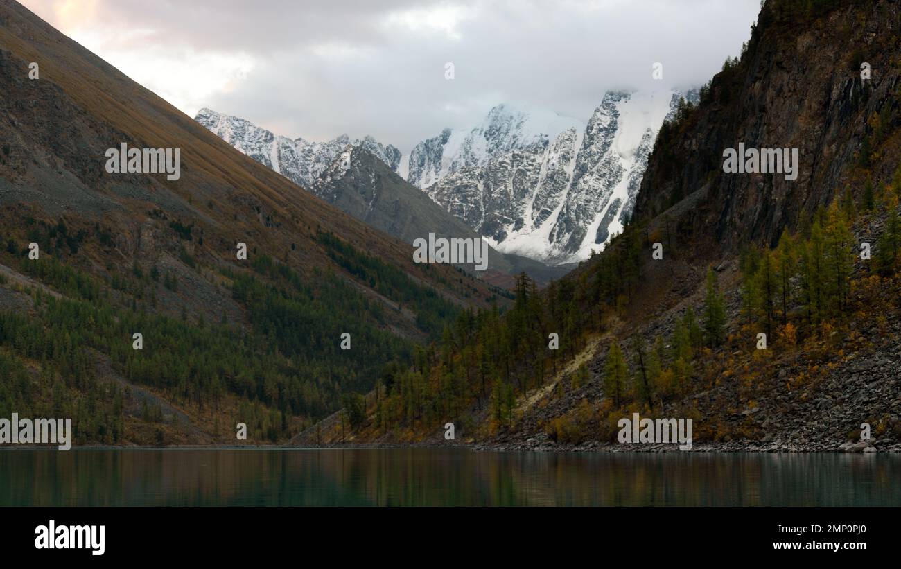 Wolken bedecken die Gipfel der hohen Berge mit Schnee und Gletschern in Altai im Schatten des Shavlinskoye-Sees im Herbst. Stockfoto