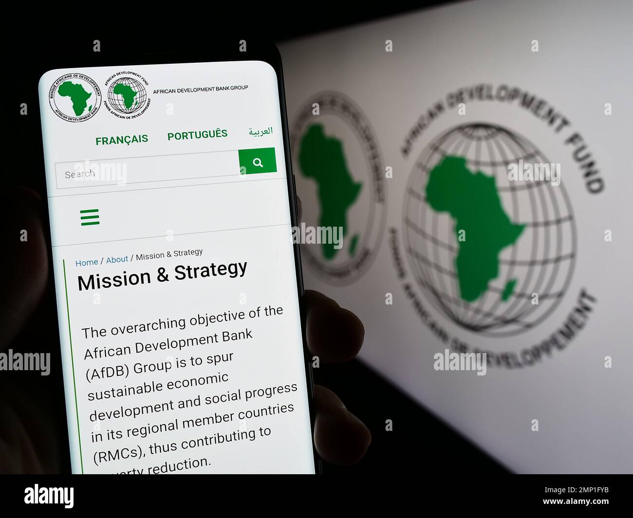 Person mit Mobiltelefon und Website der African Development Bank Group (AfDB) auf dem Bildschirm vor dem Logo. Konzentrieren Sie sich auf die Mitte des Telefondisplays. Stockfoto
