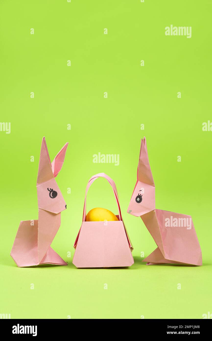 Oster-Origami - zwei Papierhasen und ein Ei mit grünem Hintergrund. Basteln für die Feiertage, machen Sie es selbst. Stockfoto