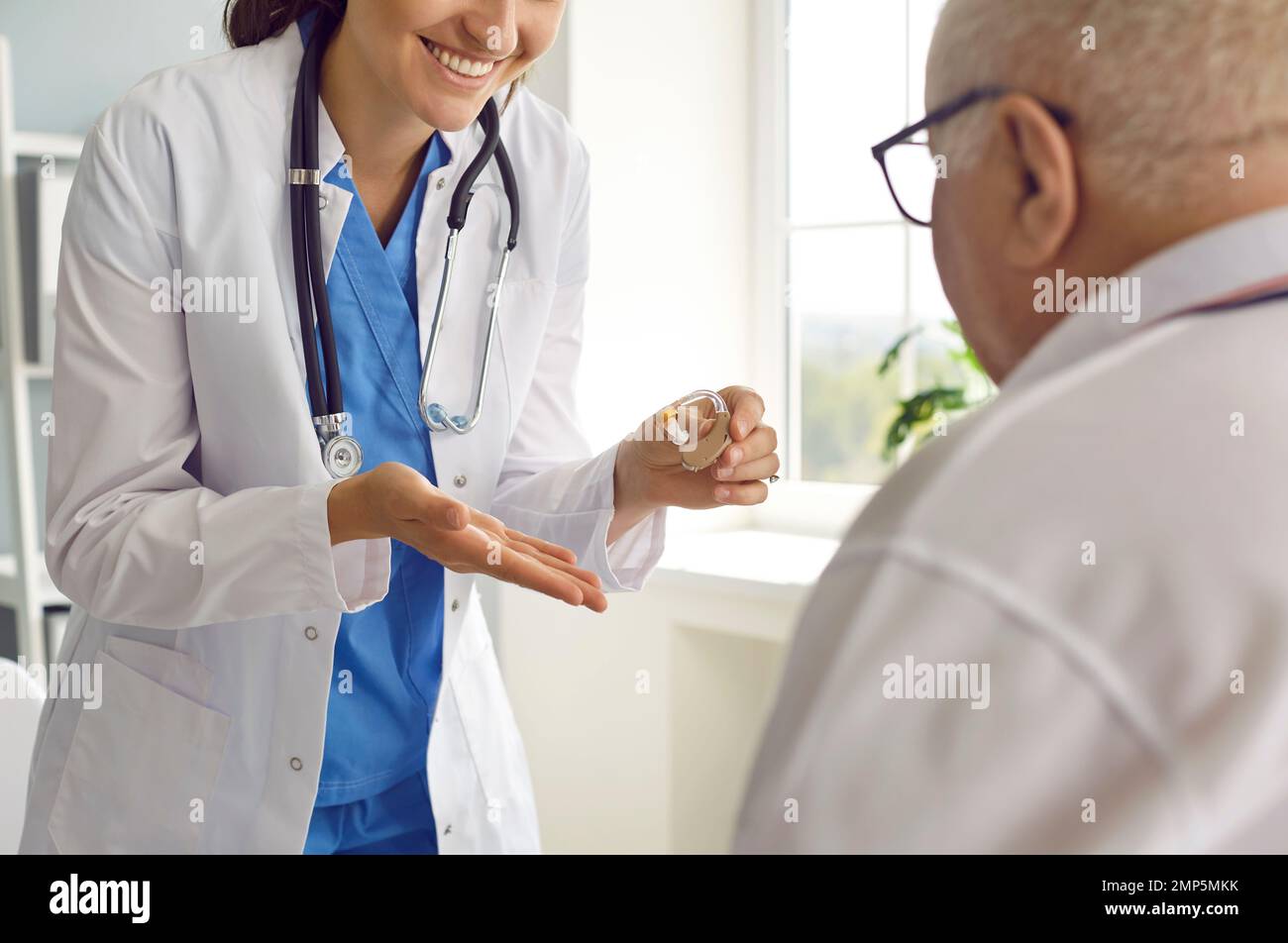 Glücklicher, lächelnder Arzt, der einem leitenden Patienten mit Hörverlust ein Hörgerät gibt Stockfoto