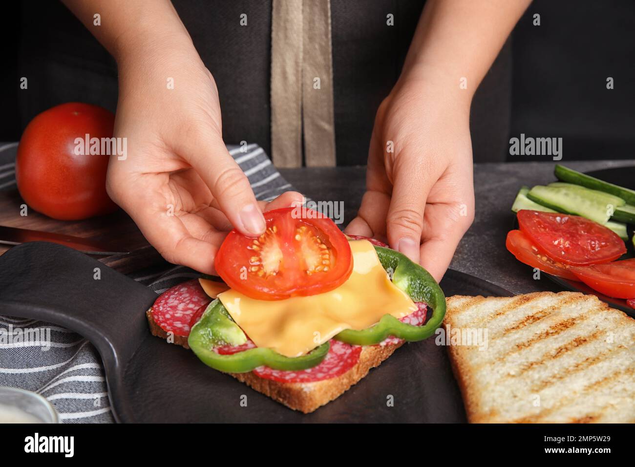 Frau, die Tomaten zum Sandwich am grauen Tisch hinzufügt, Nahaufnahme Stockfoto
