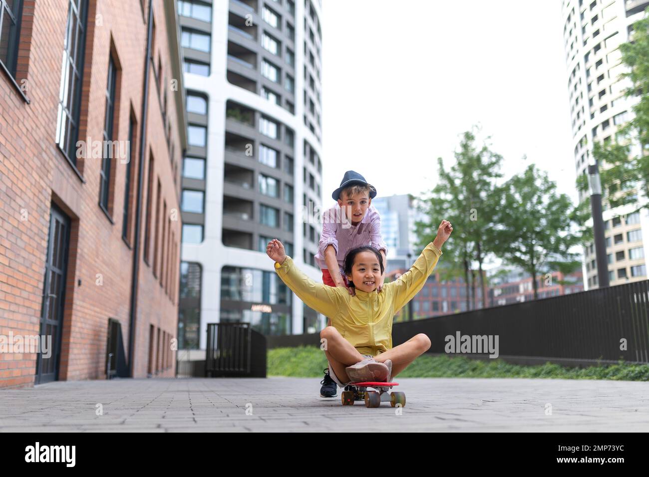 Glückliche Kinder, die eine Skateboard-Fahrt genießen und den Hügel hinunterfahren und in die Kamera schauen. Stockfoto