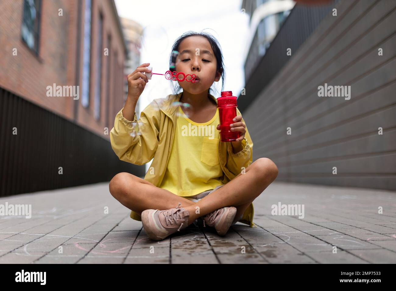 Ein kleines Mädchen, das in der Stadt sitzt und Blasen bläst. Stockfoto