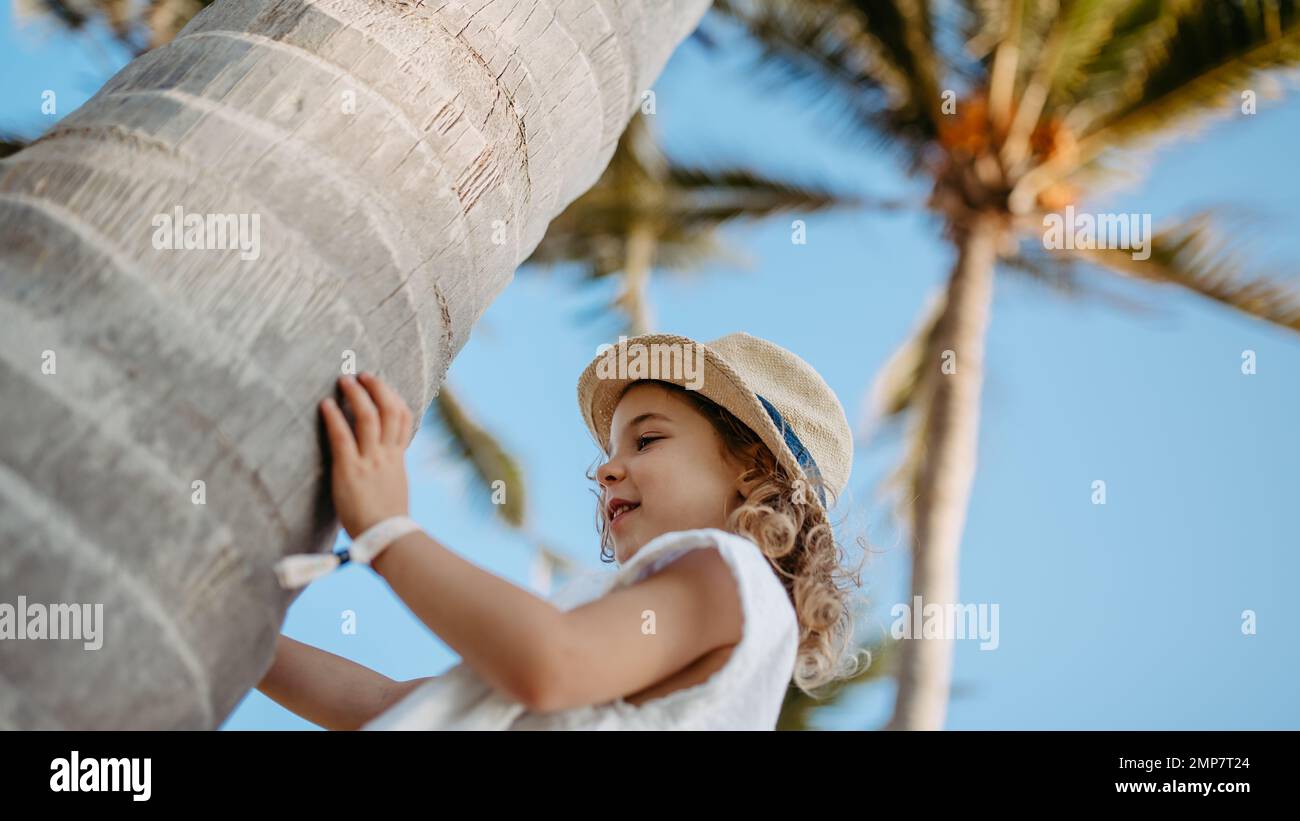Glückliches kleines Mädchen, das während des Tropenurlaubs Palmen berührt. Stockfoto