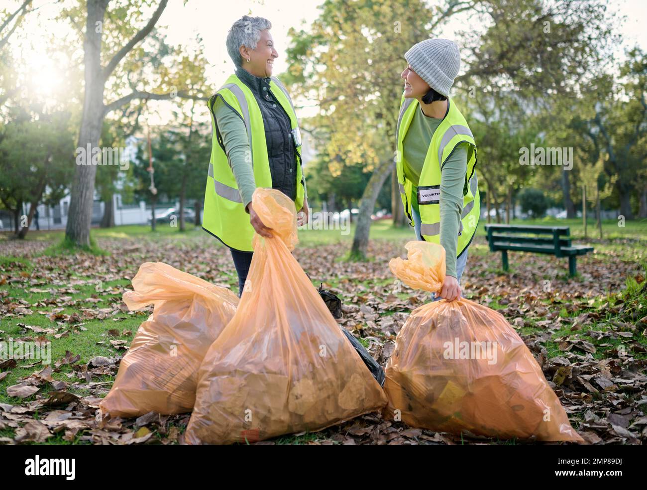 Ehrenamtliche Frauen, gemeinnützige Arbeit und Putzpark mit Müllsack für eine saubere Umgebung. Team spricht und hilft mit Müll, um umweltfreundlich zu sein Stockfoto