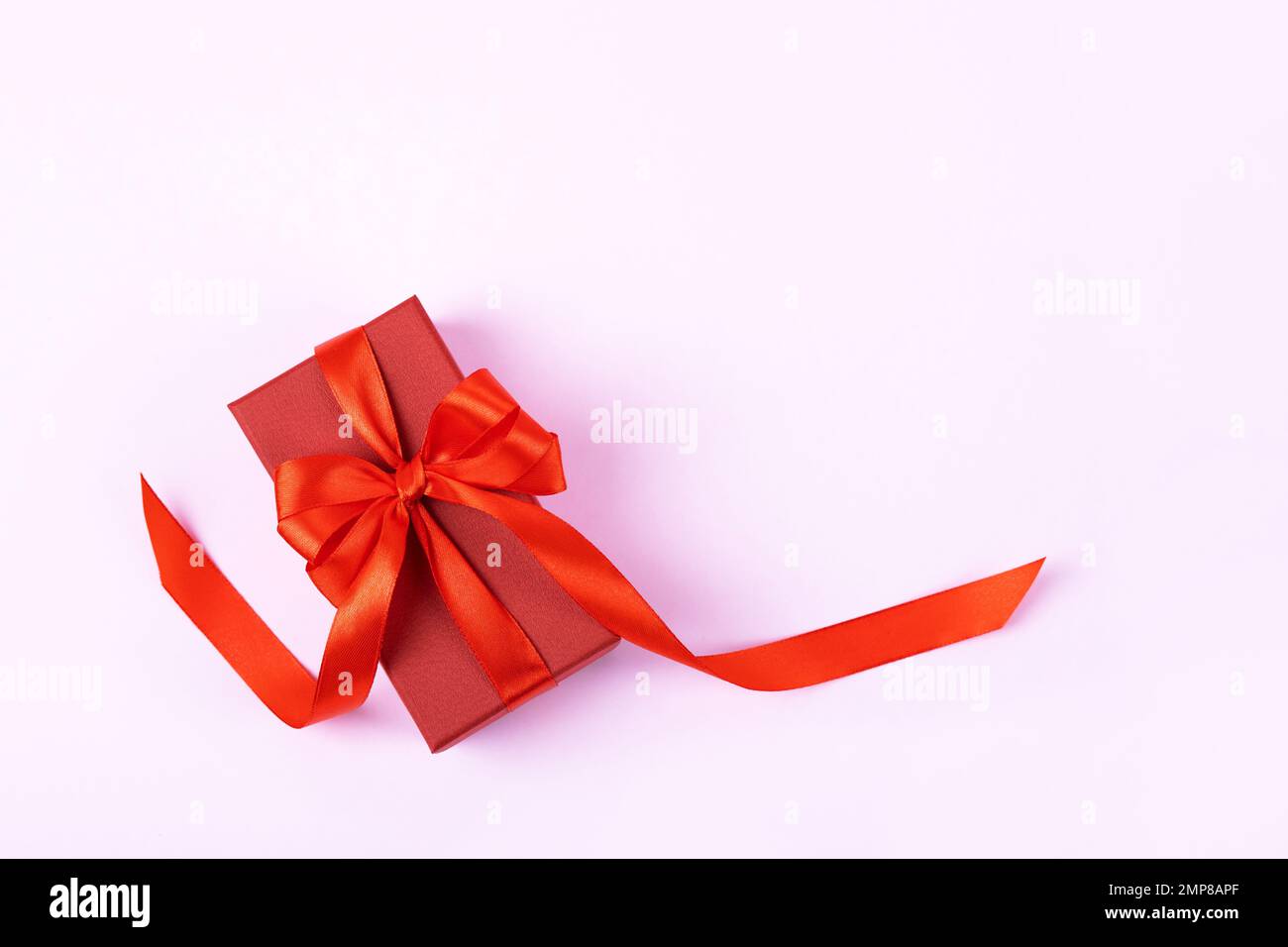 Rote Geschenkbox mit roter Schleife aus Satin auf lila Hintergrund. Grußkarte zum Valentinstag, Muttertag und Geburtstag. Stockfoto
