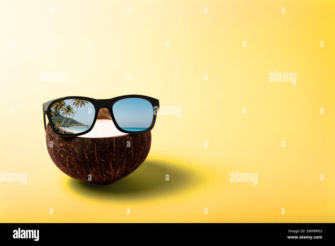 Sommerkomposition zum Thema Urlaub. Lustige Kokosnuss mit Sonnenbrille auf sonnigen gelben Hintergrund. Reflexion von Palmen und dem Ozean im Stockfoto