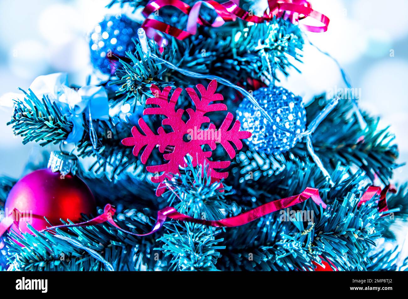 Nahaufnahme eines kleinen Weihnachtsbaums mit roten Kugeln, Ketten und einer roten Schneeflocke. Kalte Farben in Winterstimmung Stockfoto