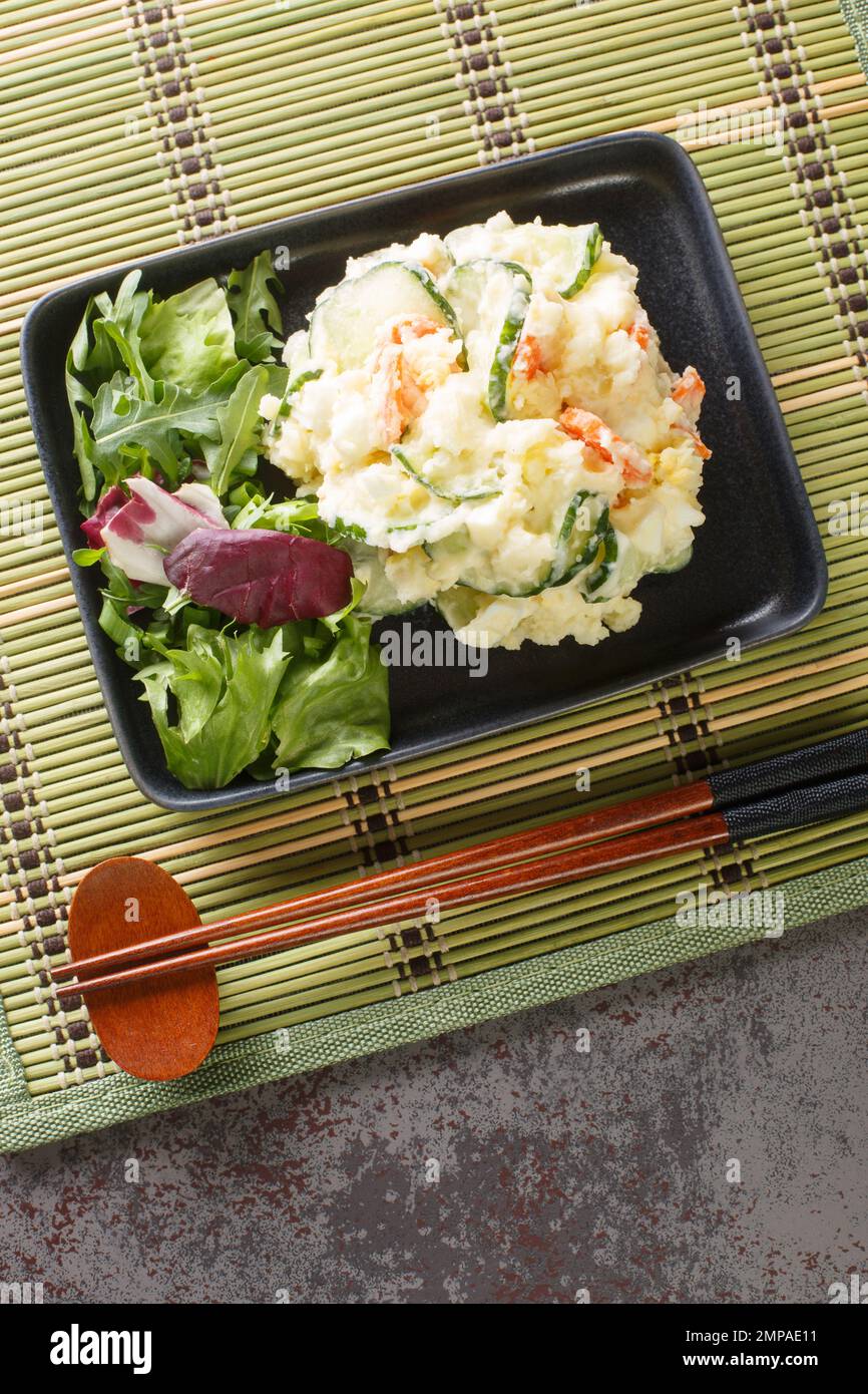 Japanischer Kartoffelsalat mit Karotten, Eiern und frischer Gurke, Nahaufnahme auf einem Teller auf dem Tisch. Vertikale Draufsicht von oben Stockfoto