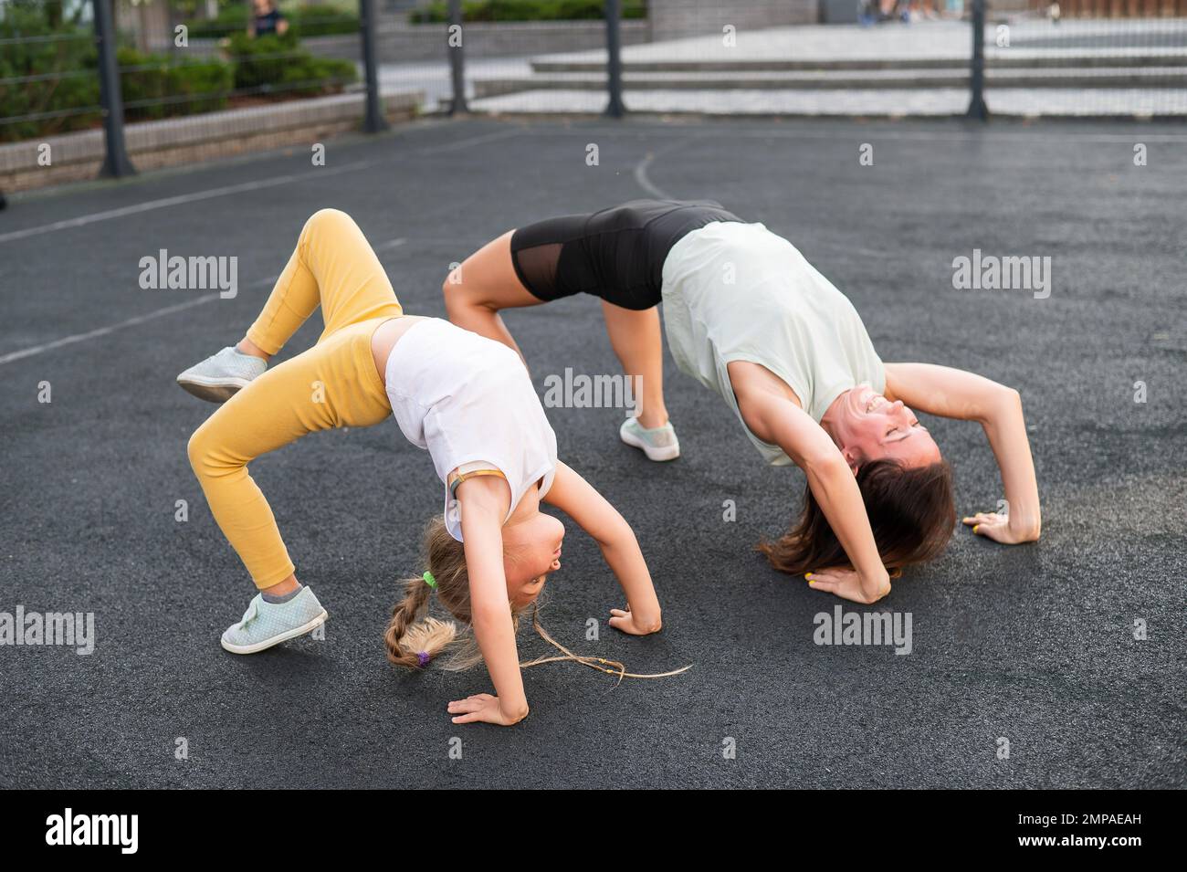 Ein kleines Mädchen und ihre Mutter machen eine Brückenübung auf dem Outdoor-Sportplatz. Stockfoto