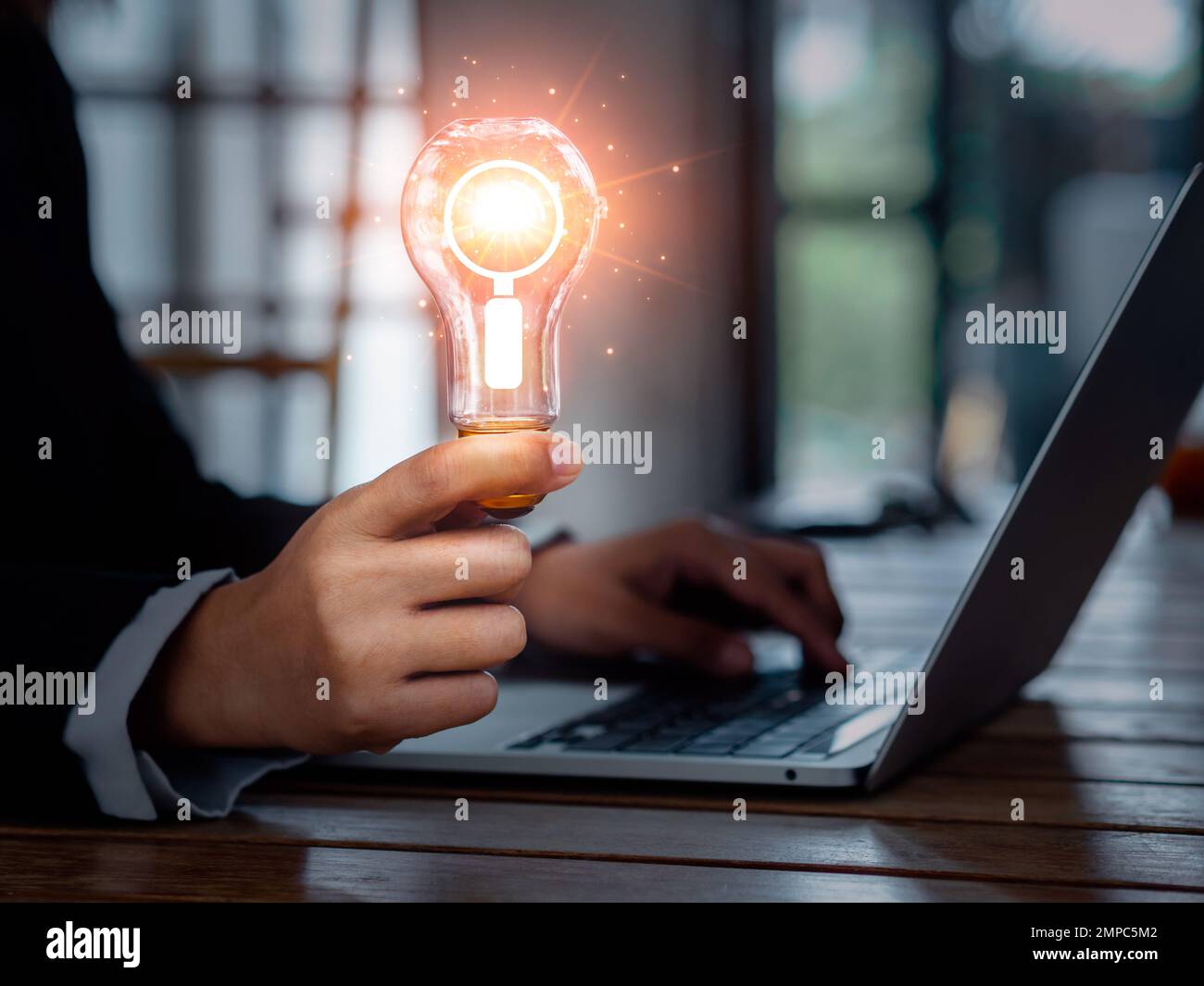 Onlinekonzept wird gesucht. Lupensymbol in einer kreativen Glühbirne, die von einem Geschäftsmann gehalten wird, der mit einem Laptop arbeitet. Digital Stockfoto