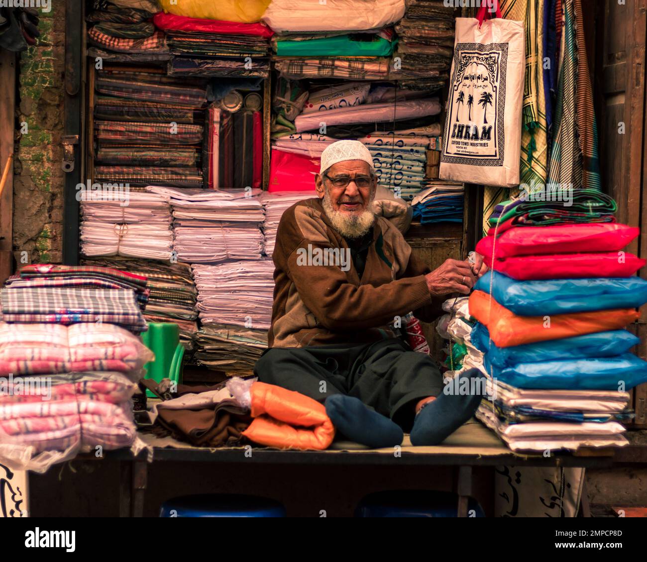 Lahore Pakistan 2020, ein alter Mann, der Tücher in seinem kleinen Stoffladen in der ummauerten Stadt Lahore verkauft, ein alter Mann, der lächelt und in die Kamera schaut Stockfoto