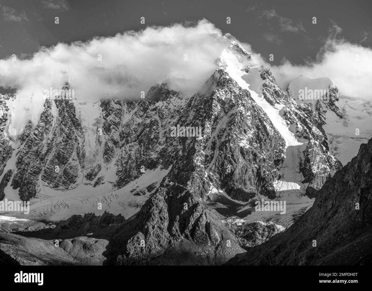 Schwarzweißfoto von Berggipfeln mit Schnee und Gletscherzungen mit weißen Wolken und Nebel in Altai im Schatten. Träume und Geschichten der Berge. Stockfoto