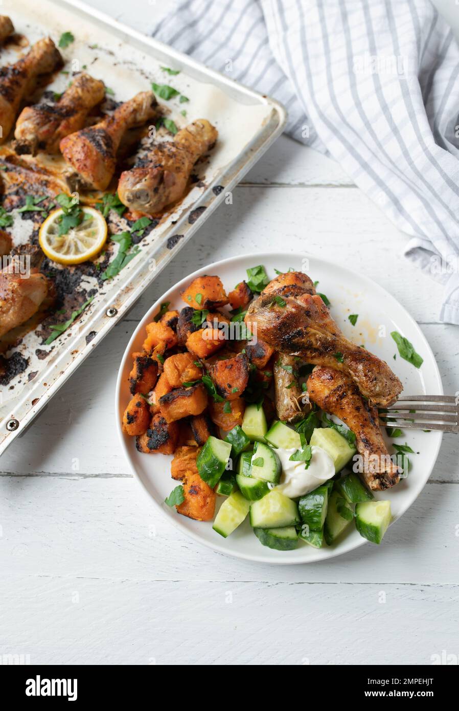 Leichtes Abendessen oder Mittagessen mit im Ofen gebackenen Hähnchenschenkeln, gerösteten Süßkartoffeln und Gurkensalat Stockfoto