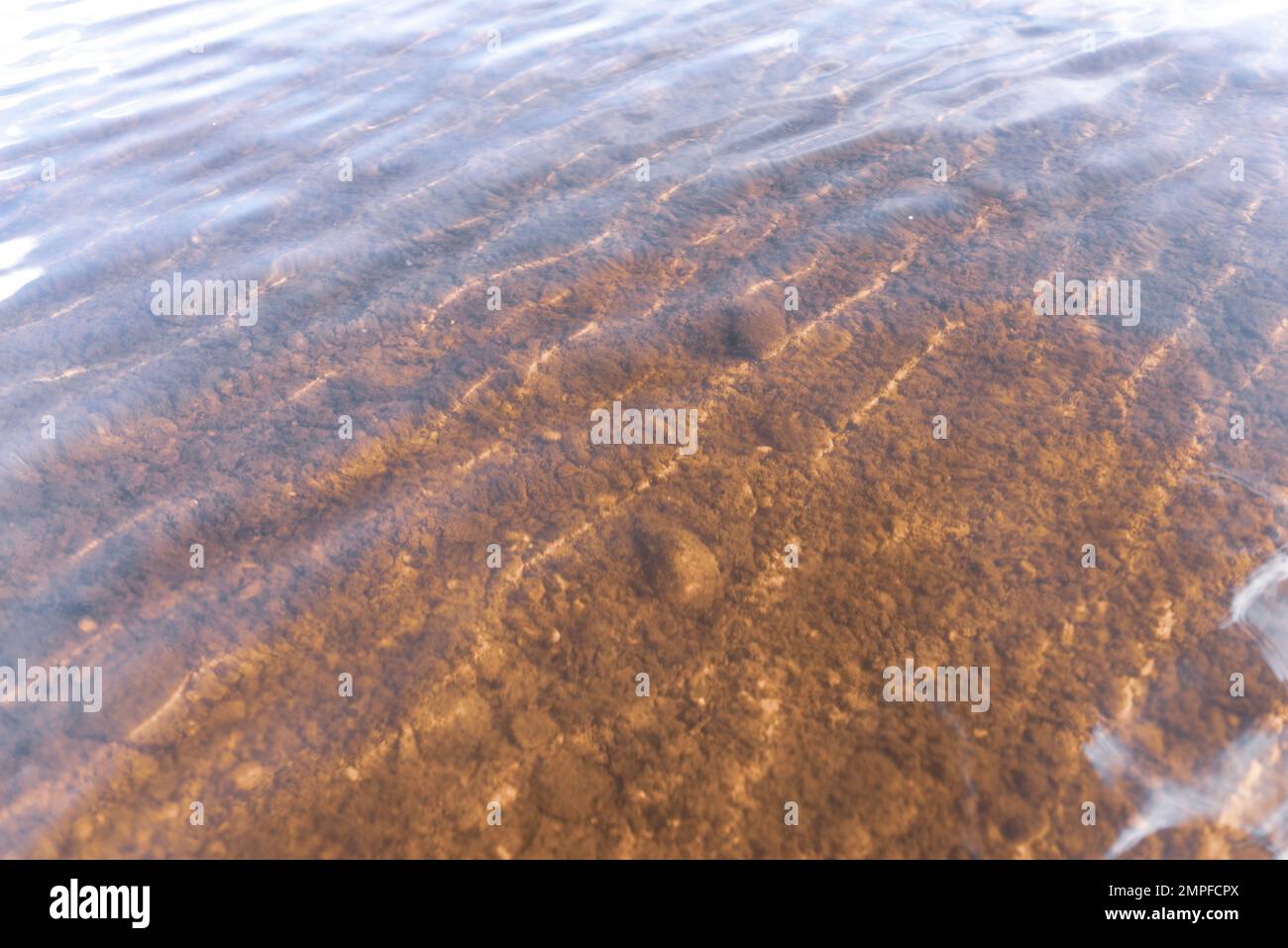 Der Grund des Flusses durch transparentes Wasser mit Lichtreflexion und Wellenbewegung. Natürliche Textur, Hintergrund. Stockfoto