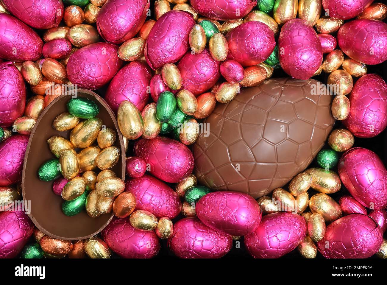 Stapel oder Gruppe von mehrfarbigen und verschiedenen Größen von bunten Folie verpackt Schokolade ostereier in rosa, rot, Gold und lime grün mit zwei Hälften o Stockfoto