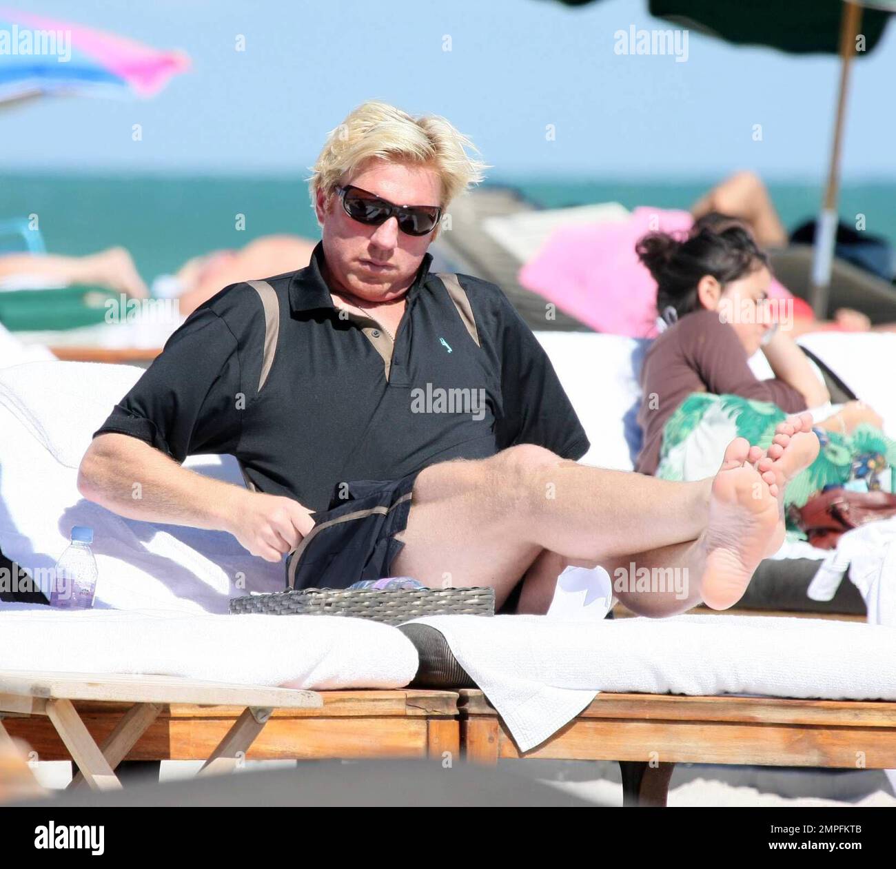 Nur wenige Tage, nachdem sich das Tennisspiel Boris Becker aufgrund einer Rückenverletzung von der Stanford-Meisterschaft zurückgezogen hat, sieht man ihn in Miami Beach mit einem Freund entspannen. Der dreimalige Wimbledon-Champion sollte letzte Woche seit 1999 sein erstes Spiel in den USA im Turpin Tennis Center der SMU spielen, aber er konnte seine Trainingseinheit nicht abschließen und wurde durch Justin Gimelstob ersetzt. Becker hat wahrscheinlich noch Schmerzen, zog ein paar lustige Gesichter, während er mit seinem Oberteil in der Sonne Floridas sonnte. Nach einer Weile zog er sich an und ging in sein Luxushotel und zog seine windgepeitschten Haare an, während er Carryi trug Stockfoto