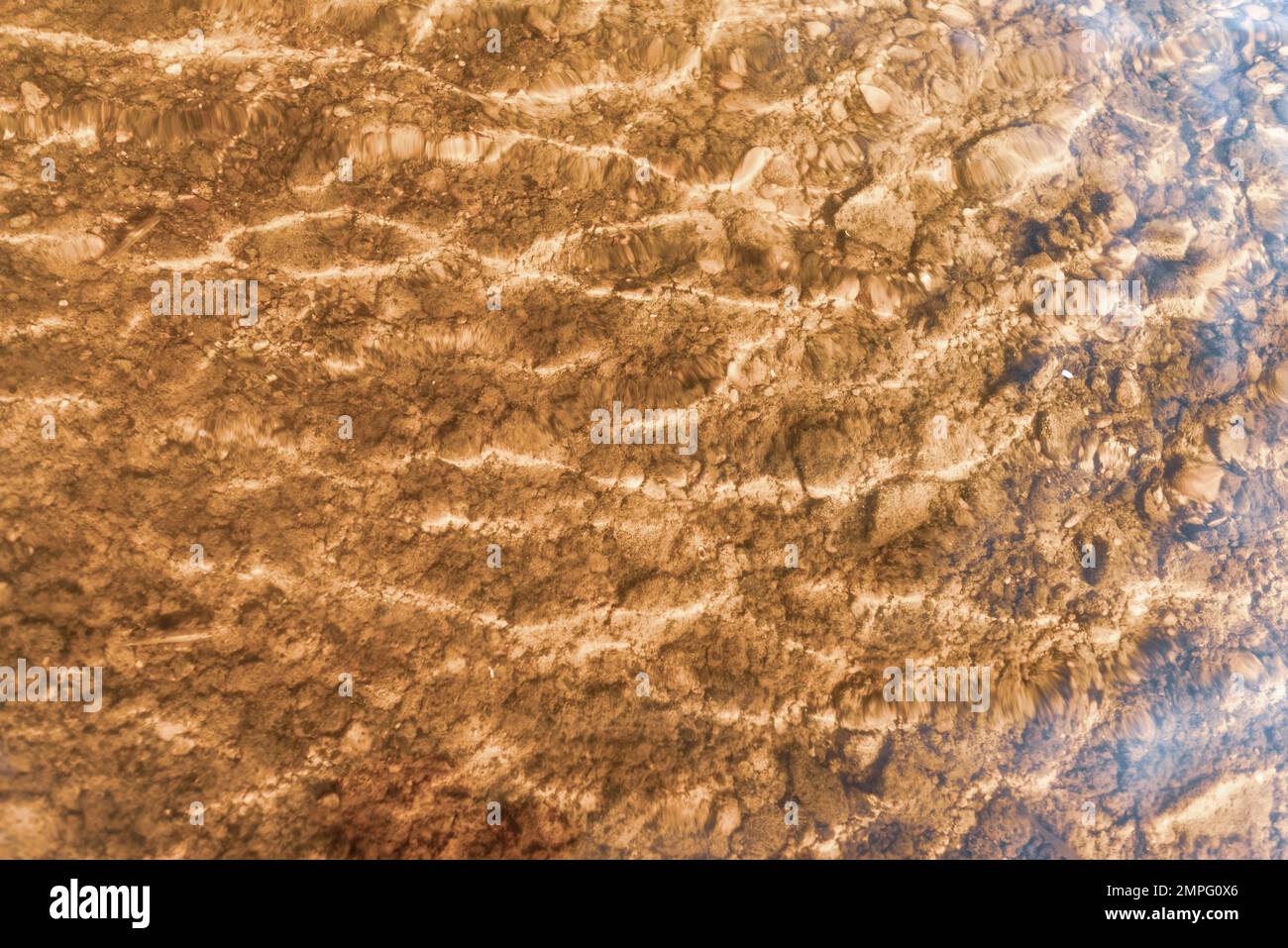 Abstraktes Foto der Wasseroberfläche mit Steinen am Boden und Reflexion auf den Wellen in leuchtend roten Farben. Stockfoto