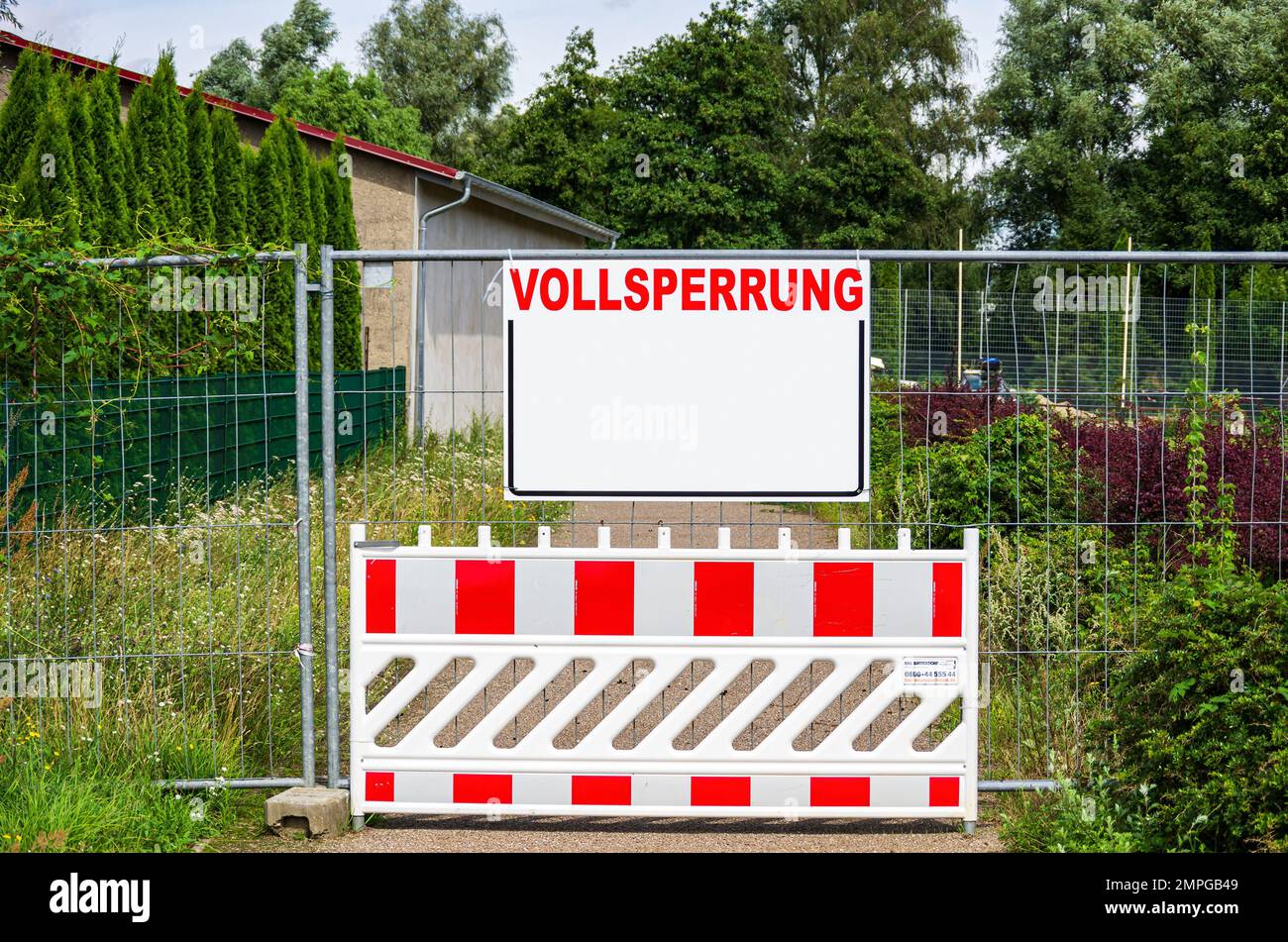 Ein geschlossener Weg mit einer Barriere und einem Bauzaun mit einem rechteckigen Brett mit viel Textplatz mit dem Wort VOLLSPERRUNG (Full Closure). Stockfoto
