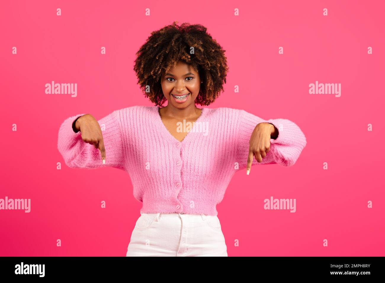 Fröhliche junge schwarze lockige Frau in lässiger Klammer mit den Fingern nach unten Anzeige und Angebot empfehlen Stockfoto