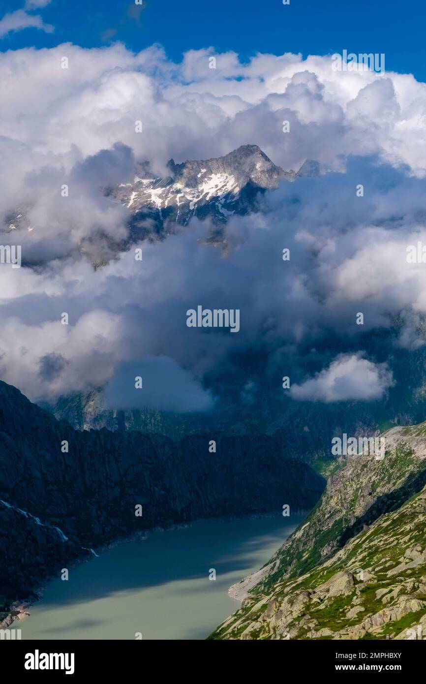 Die Gipfel der Berge Galenstock, Gärstenhörner und Dammastock, die aus den Wolken ragen, sehen Sie über dem Stausee Grimselsee. Stockfoto
