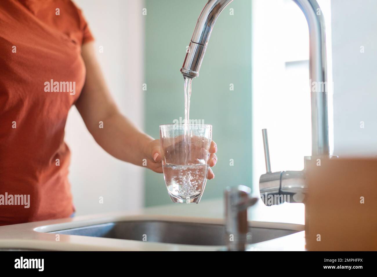 Unbekannte Frau, Die Glas Mit Wasser Aus Dem Wasserhahn In Der Küche Füllt Stockfoto