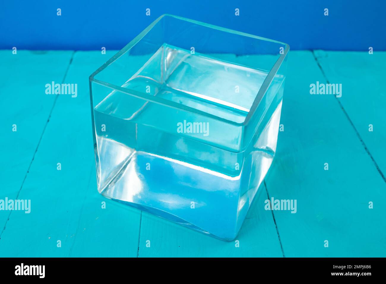 Glaswürfel gefüllt mit Wasser auf blauem Hintergrund, Nahaufnahme mit weichem Fokus Stockfoto