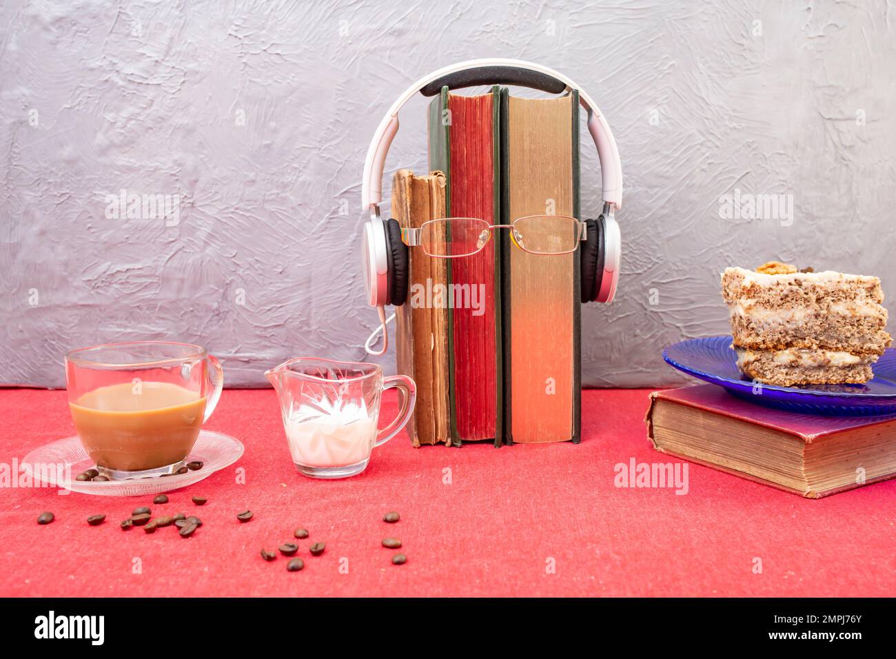 Schreibtisch mit roter Tischdecke, Kaffee, Kuchen, Büchern, Lesebrillen und Kopfhörern Stockfoto