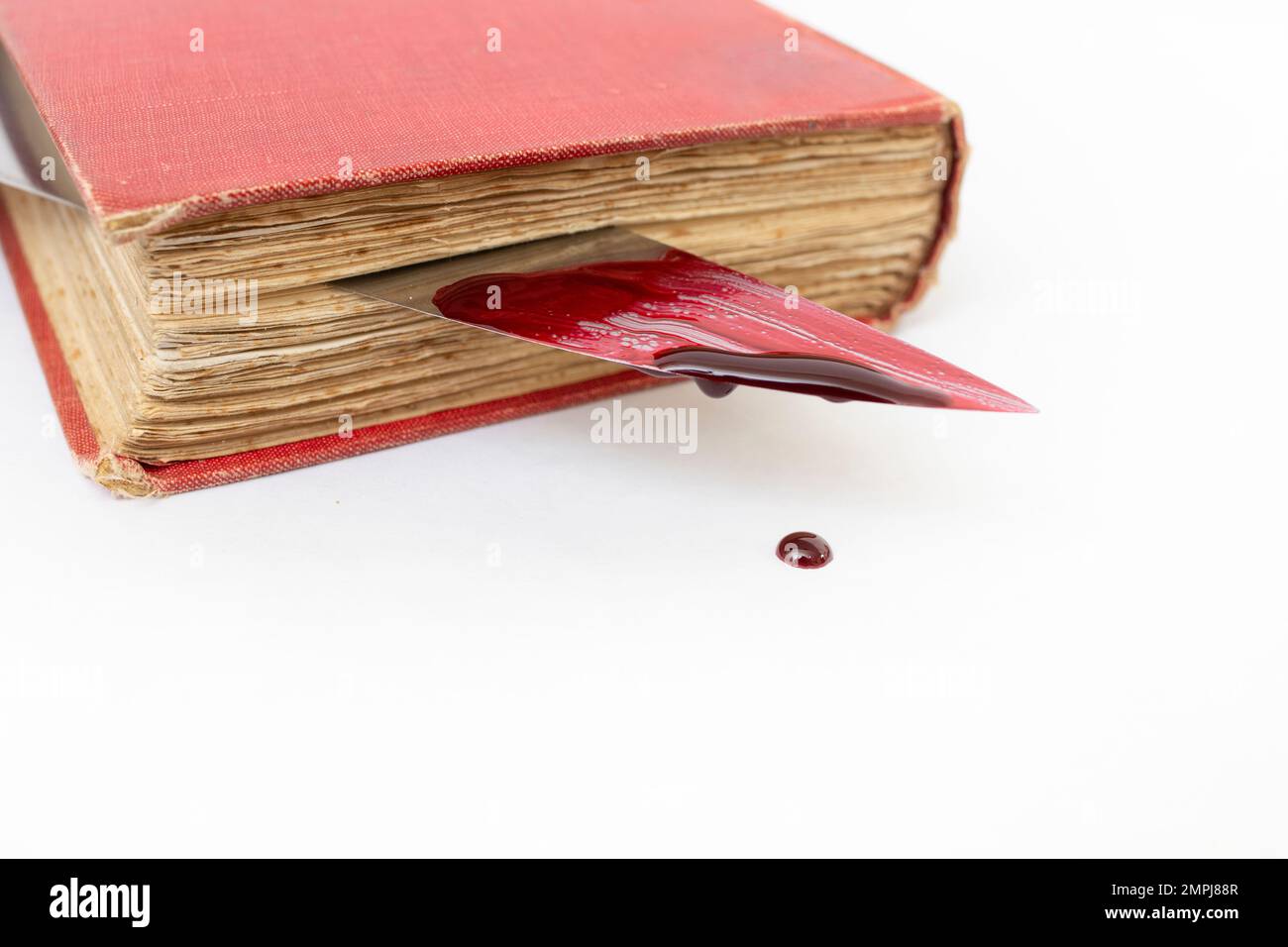 Blutiges Messer zwischen den Seiten eines alten Buches, mit tropfender roter Farbe, weicher Nahaufnahme Stockfoto