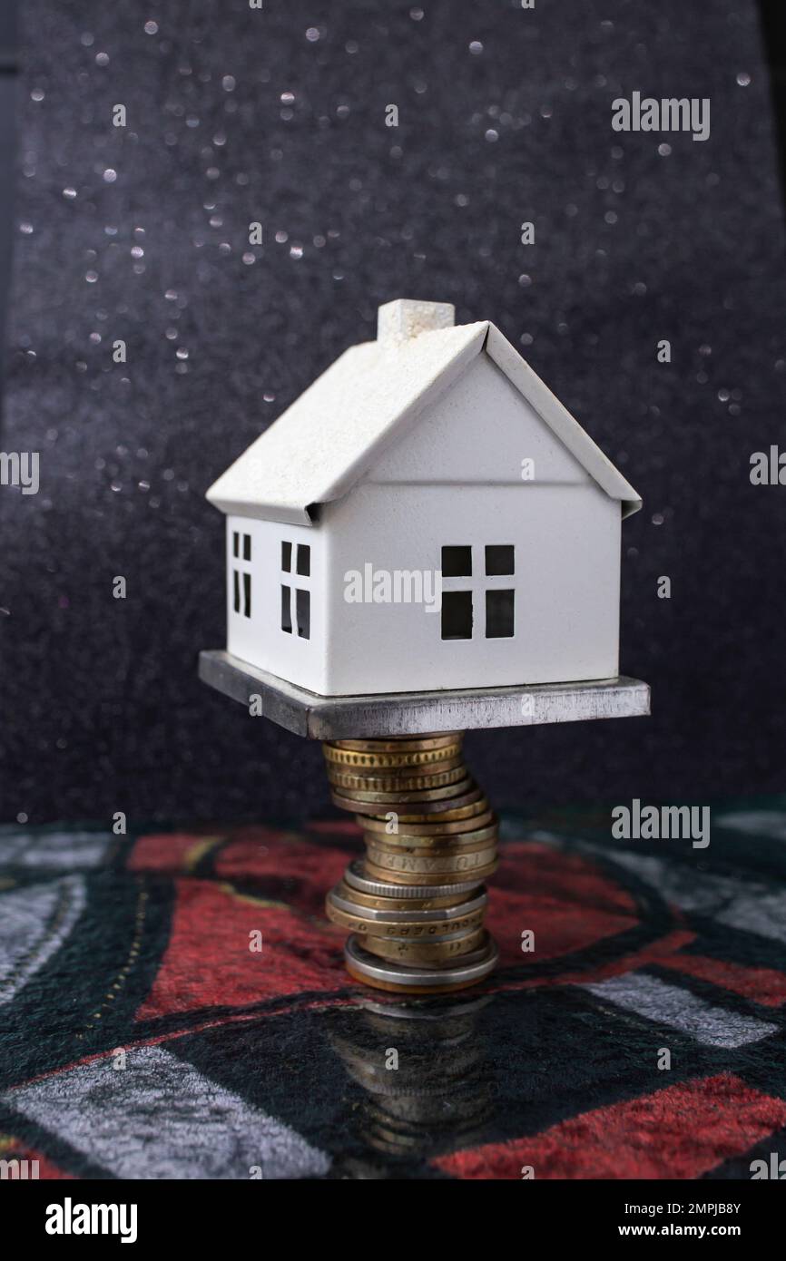 Weißes Modellhaus auf einem Münzstapel, auf dunklem Hintergrund, weiche Nahaufnahme Stockfoto