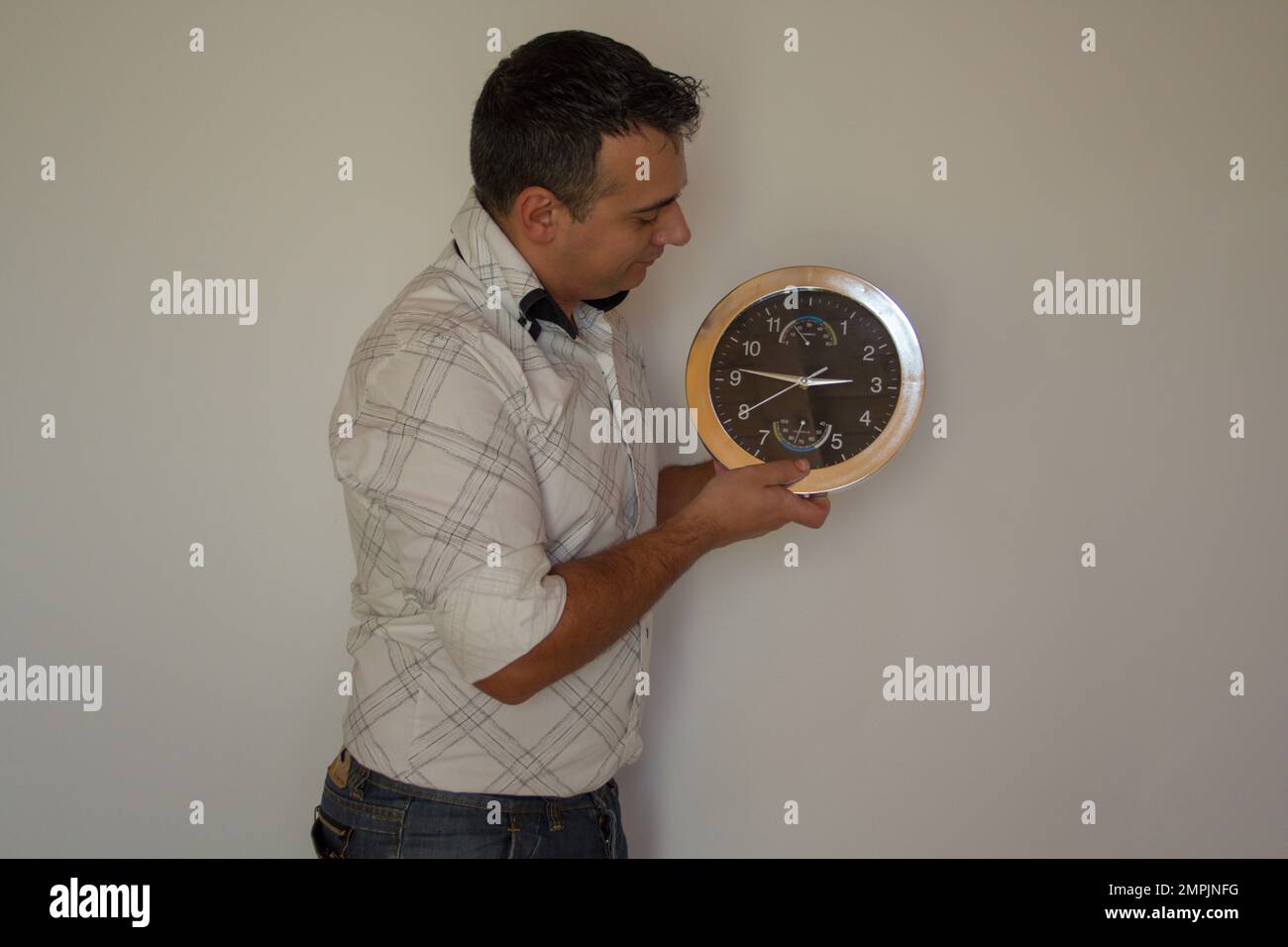 Bild eines Mannes, der eine Wanduhr hält, während er die richtige Uhrzeit einstellt. Stockfoto