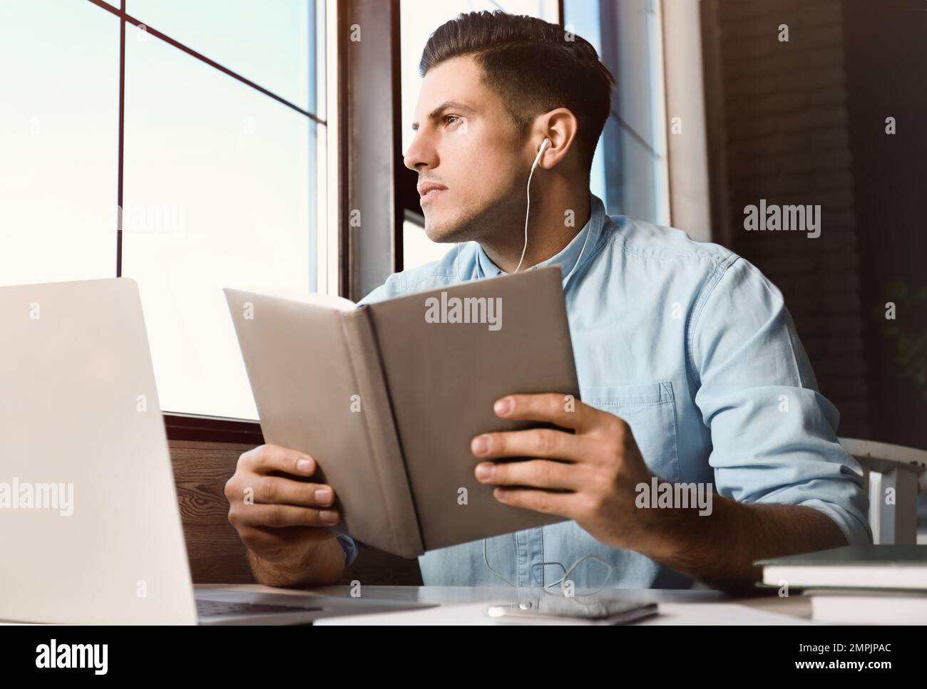 Ein Mann, der am Tisch im Café Hörbücher hört Stockfoto