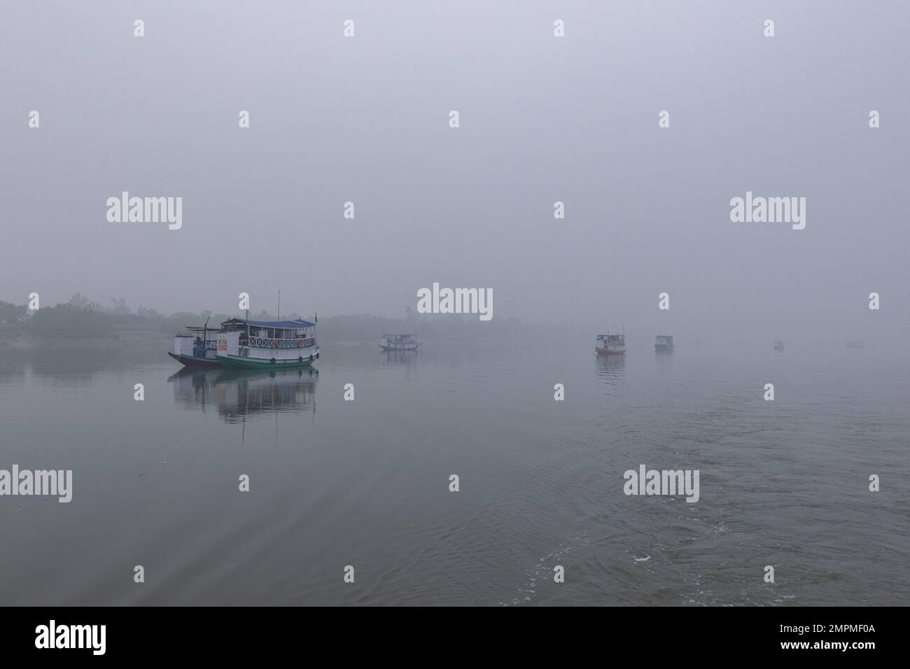 Fischerboote, die einen Fluss in Sunderbans an einem nebligen Wintermorgen versorgen Stockfoto