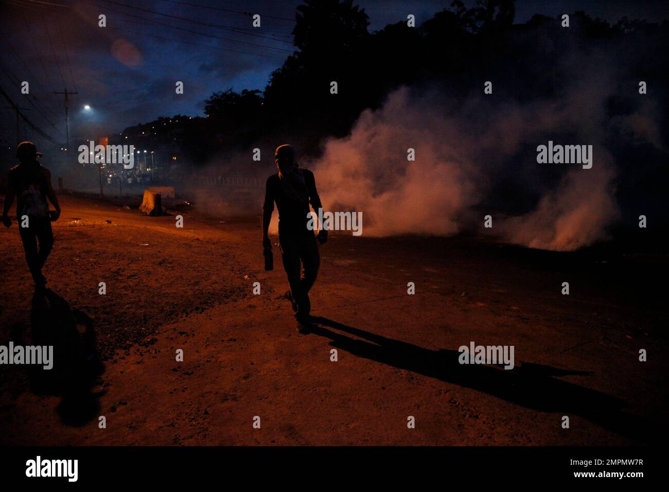 Supporters of presidential candidate Salvador Nasralla walk among tear gas fired by police as they protest alleged election fraud in Tegucigalpa, Honduras, Friday, Dec. 1, 2017. As the wait for Sunday's election results has dragged on, rock-wielding protesters have increasingly taken to the streets against riot police armed with tear gas, batons and water cannons. (AP Photo/Fernando Antonio) Stockfoto