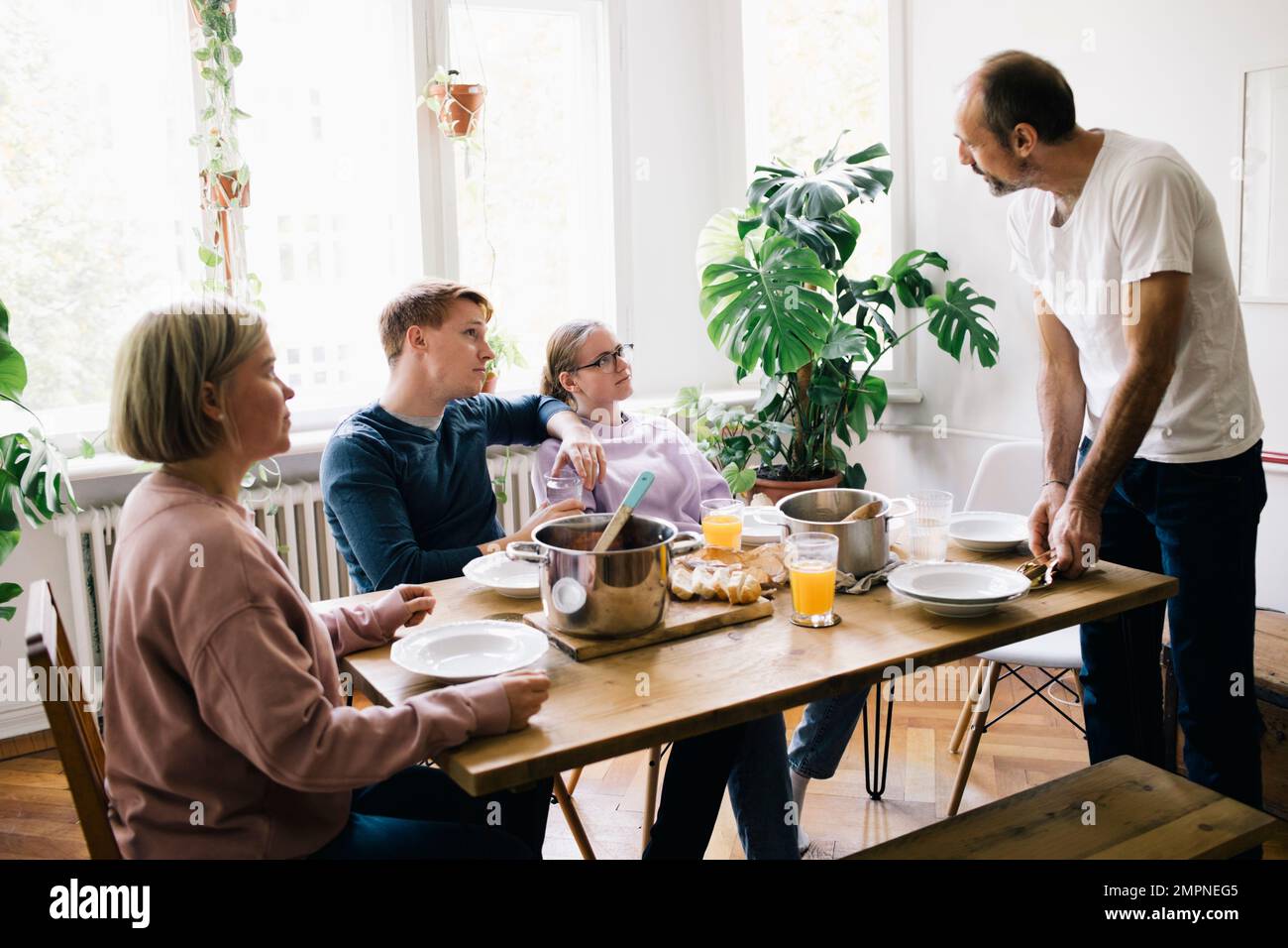 Familie, die sich mit Dad unterhält, der zu Hause am Tisch steht Stockfoto