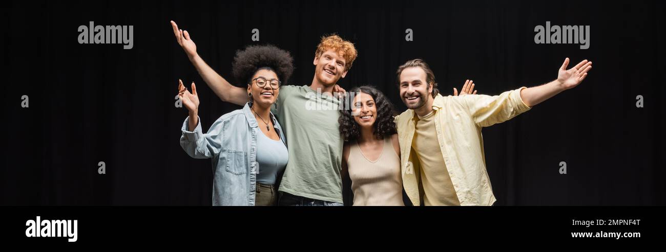 Eine Truppe von lächelnden multikulturellen Schauspielern, die sich im Theater umarmen und mit den Händen winken, Banner Stockfoto