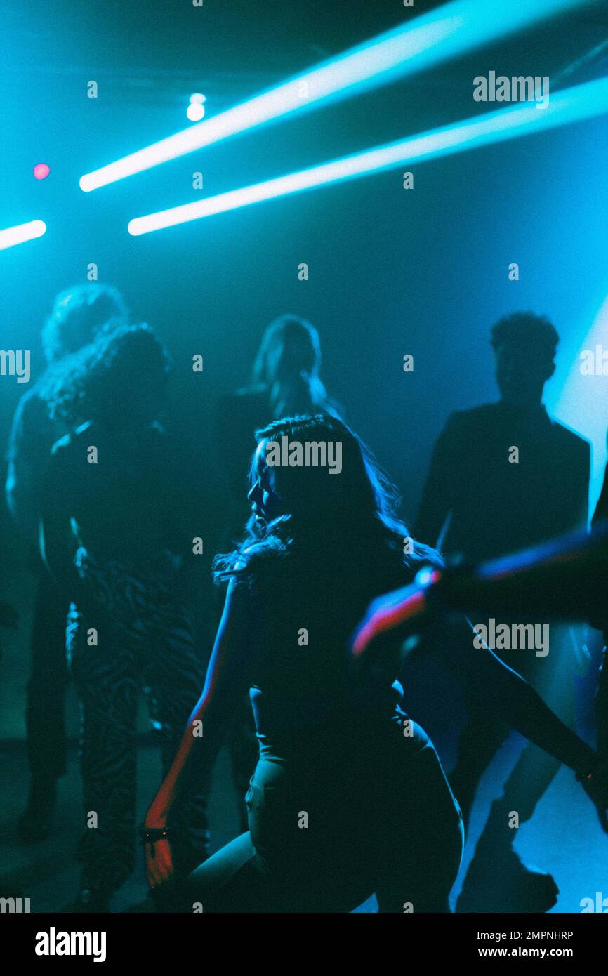 Rückansicht einer jungen Frau, die in der Nähe von Freunden auf der Tanzfläche im Nachtclub tanzt Stockfoto