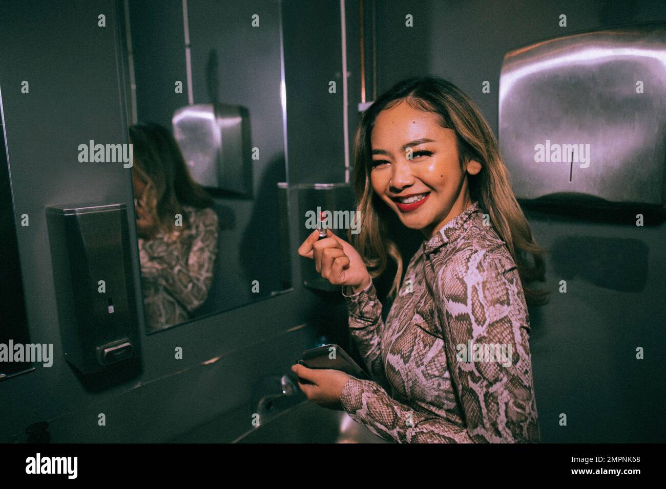 Porträt einer lächelnden jungen Frau, die Lippenstift im Bad im Nachtclub aufträgt Stockfoto