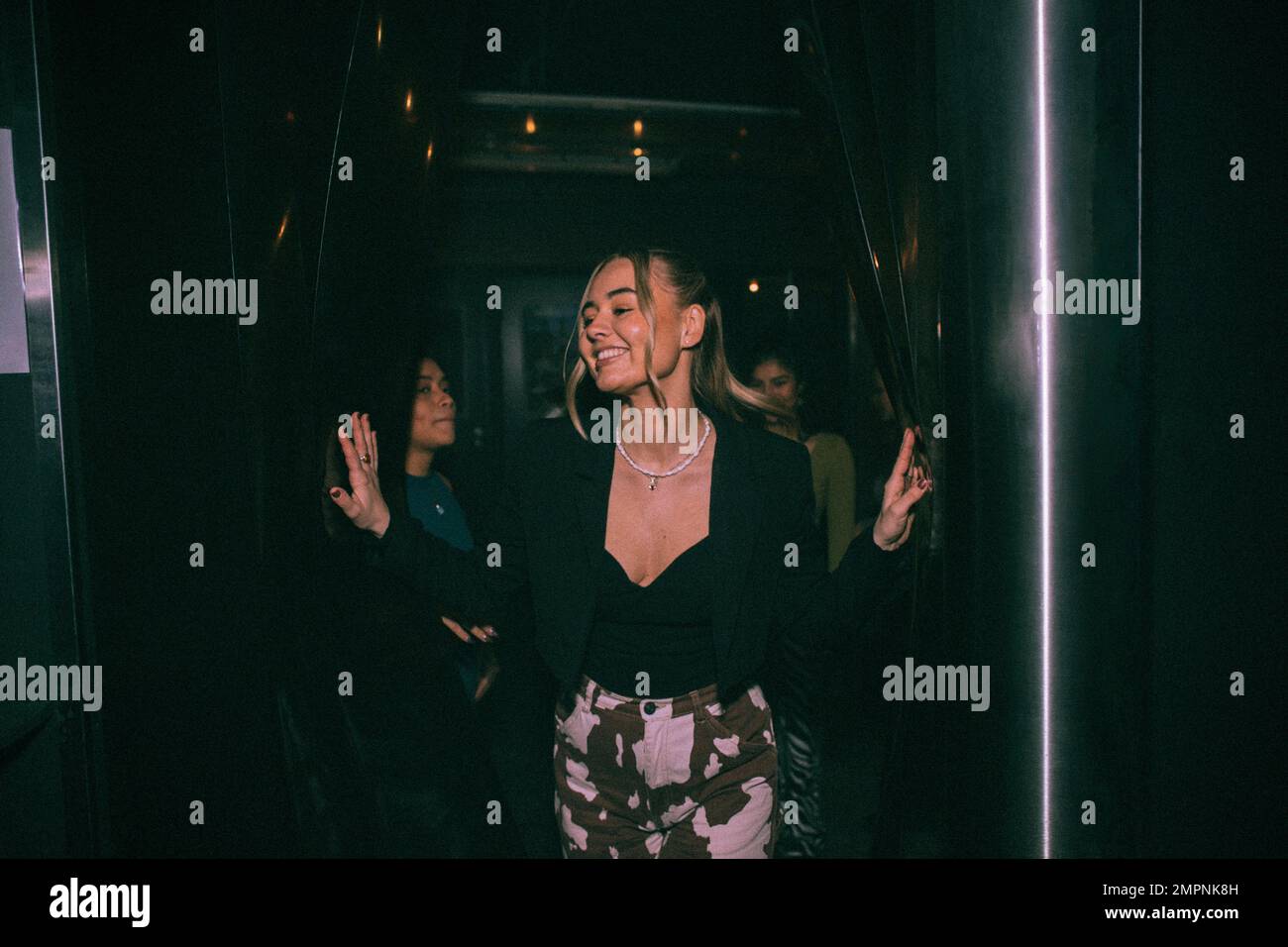 Fröhliche junge Frau, die aus dem Badezimmer kommt, mit Freunden im Hintergrund im Nachtclub Stockfoto