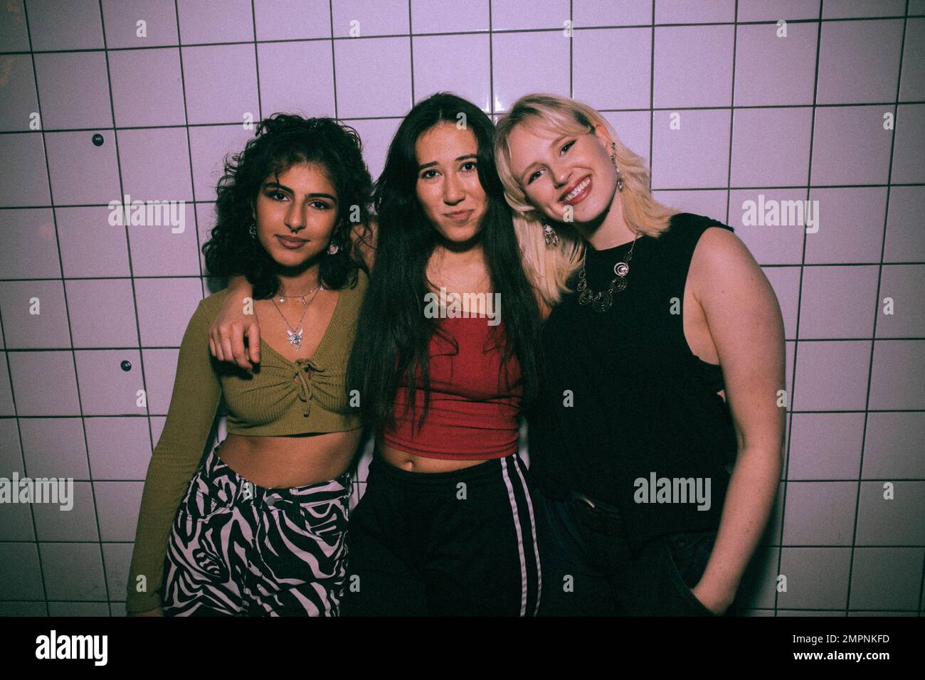 Porträt von jungen, multirassischen, weiblichen Freunden, die mit Armen gegen die weiße Wand im Nachtclub stehen Stockfoto
