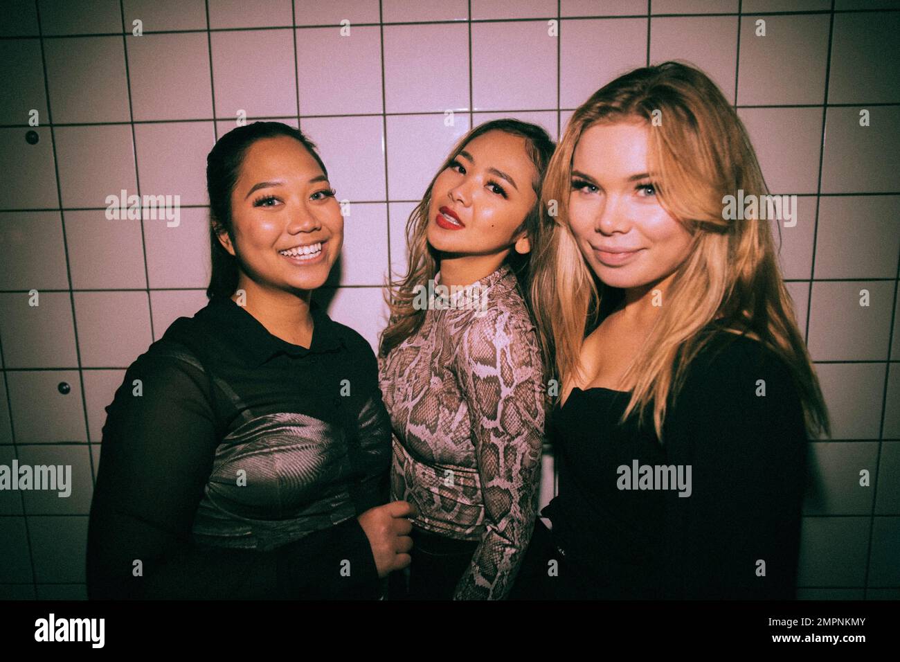 Porträt von lächelnden jungen, multirassischen, weiblichen Freunden an der weißen Wand im Nachtclub Stockfoto