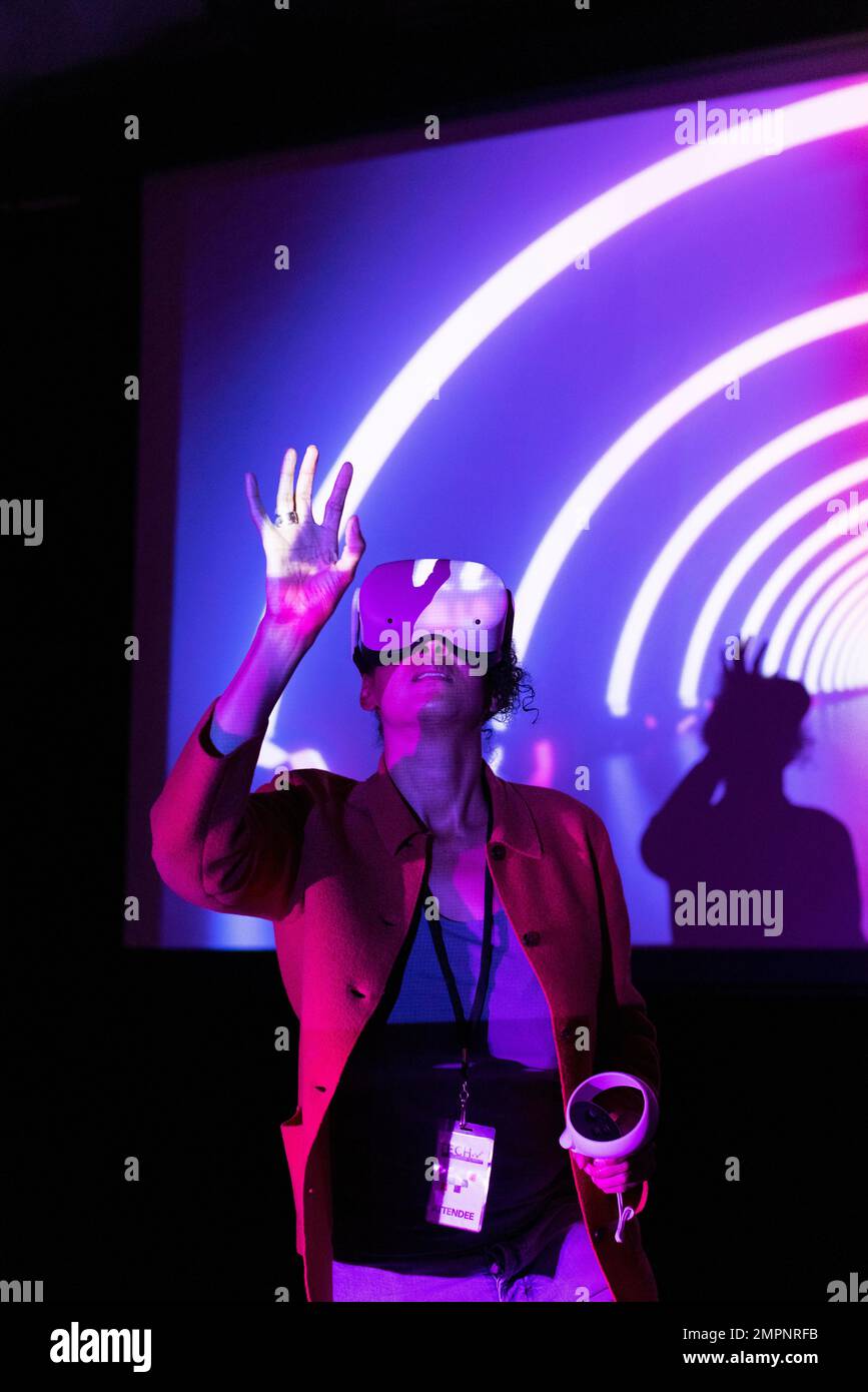 Geschäftsfrau, die eine Virtual-Reality-Brille gegen die Projektionsleinwand im Ausstellungszentrum trägt Stockfoto