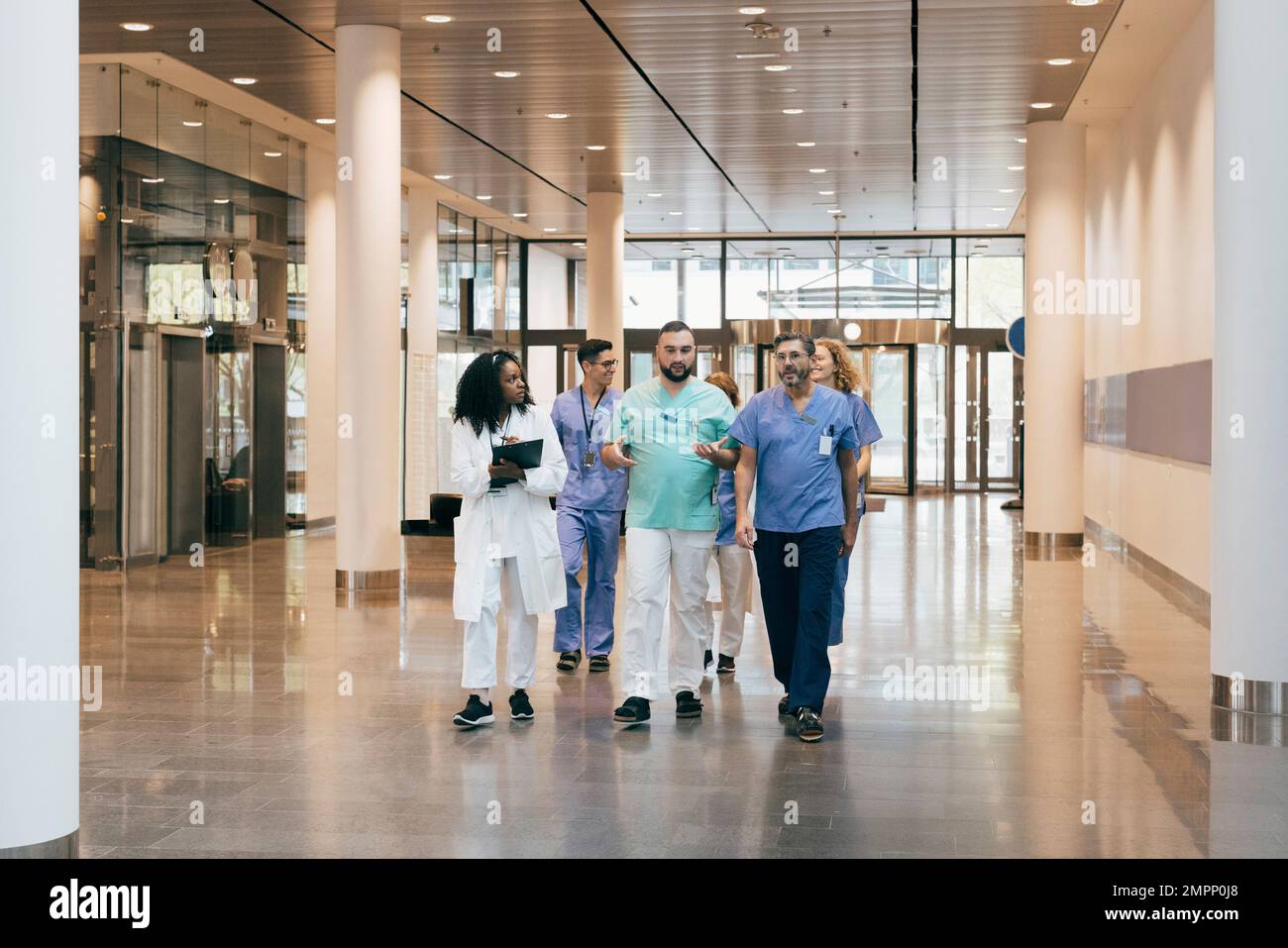 Multiethnische Gruppe von männlichen und weiblichen Krankenhauspersonal diskutiert während des Spazierens in der Lobby Stockfoto
