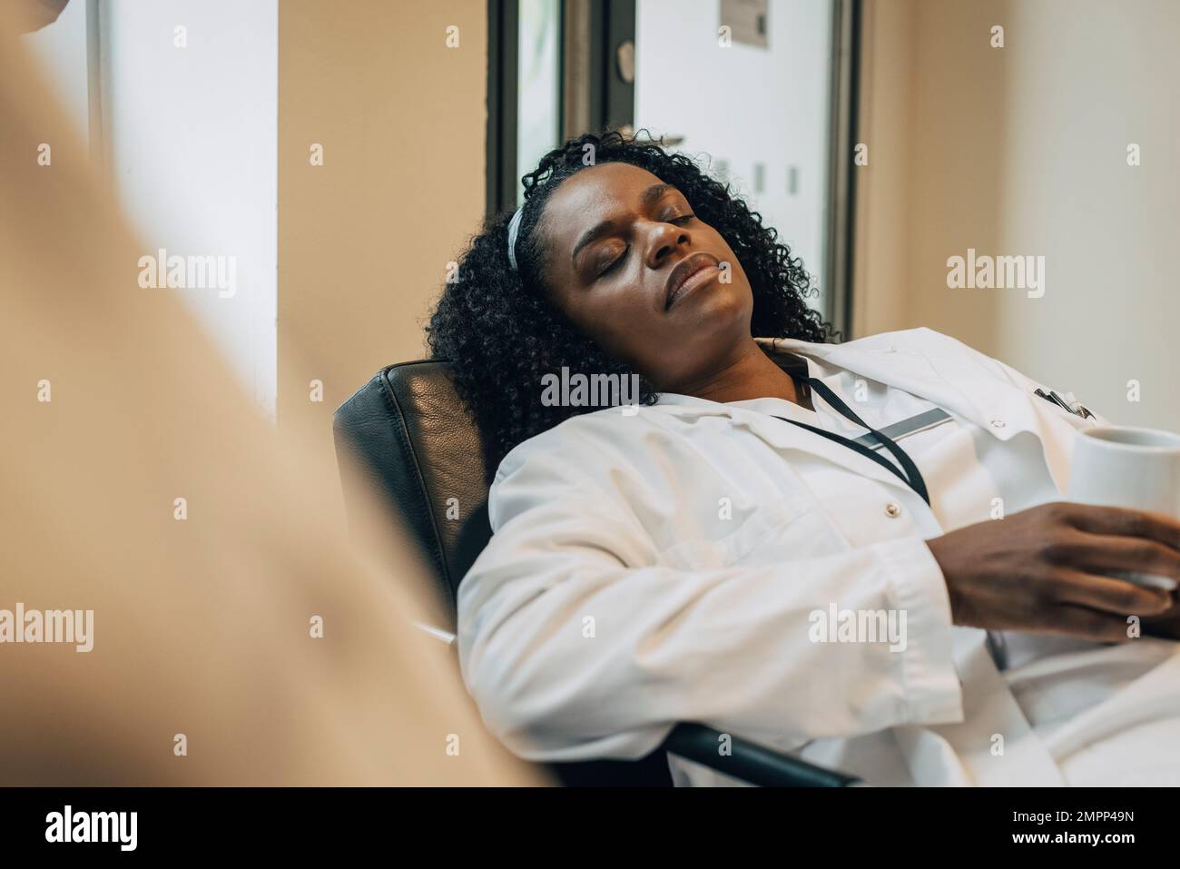 Müde Arztin, die während der Kaffeepause im Krankenhaus ein Nickerchen macht Stockfoto
